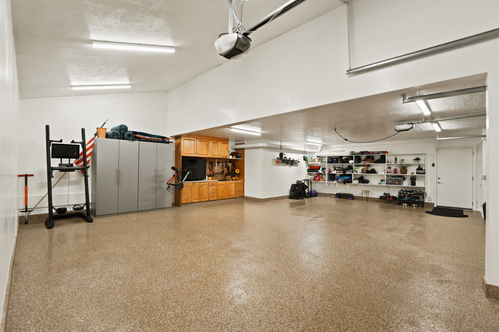 Spacious garage featuring a speckled epoxy floor, built-in wooden cabinetry, wall-mounted shelving, and bright overhead strip lighting