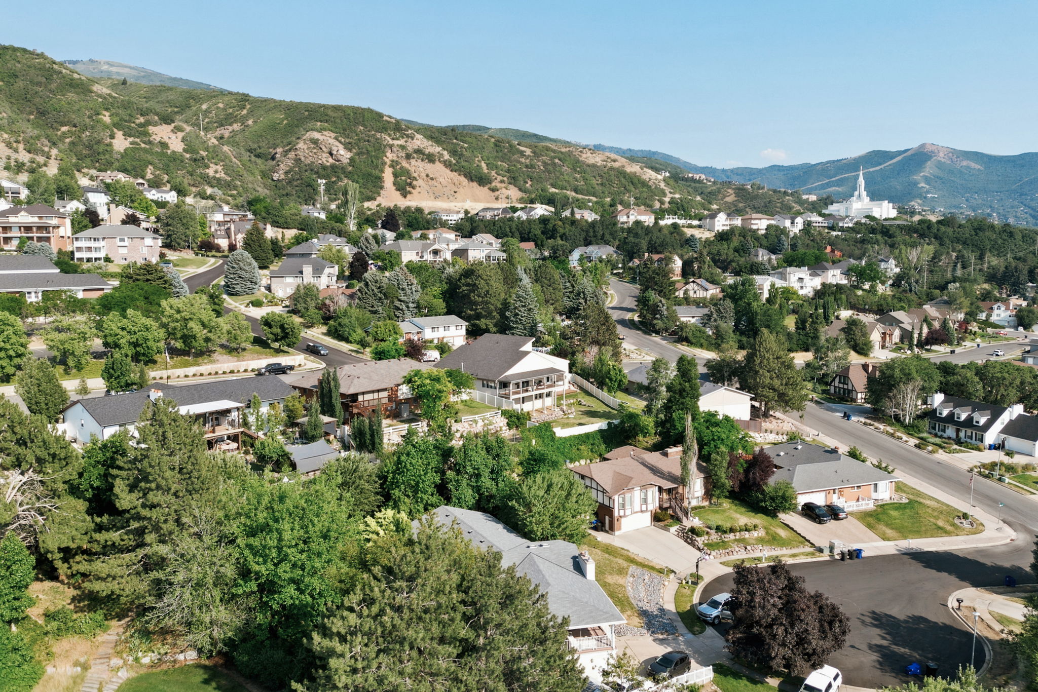Neighborhood featuring mature trees, paved streets, and mountainous terrain