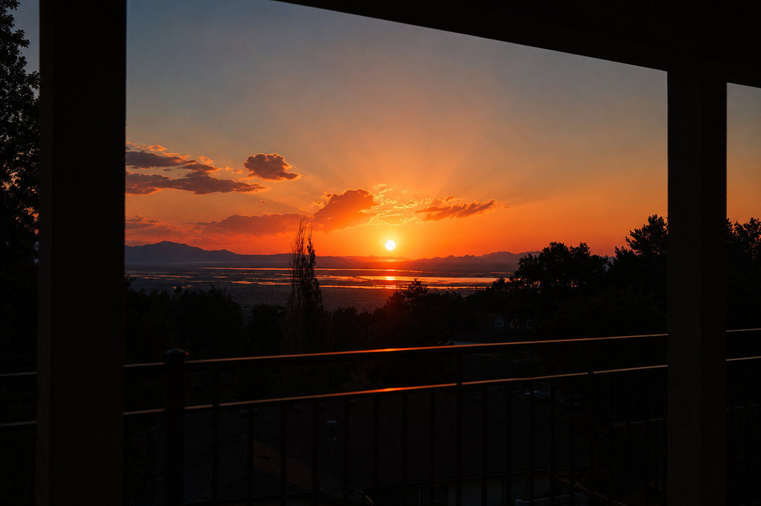 Expansive outdoor space featuring a balcony with metal railings and a panoramic sunset over a body of water with distant mountains