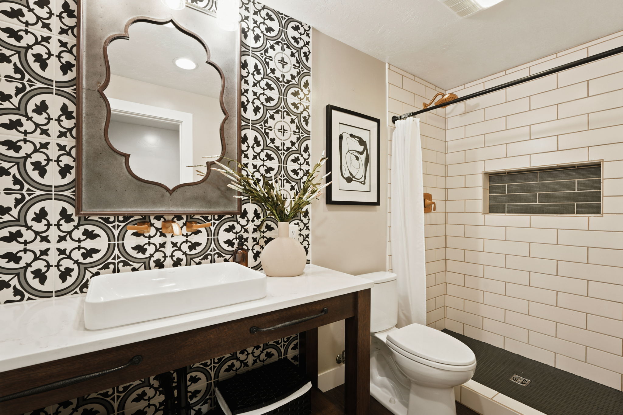 Bathroom featuring a vanity with a white countertop and rectangular vessel sink, a decorative wall mirror, and a tiled shower with a built-in niche