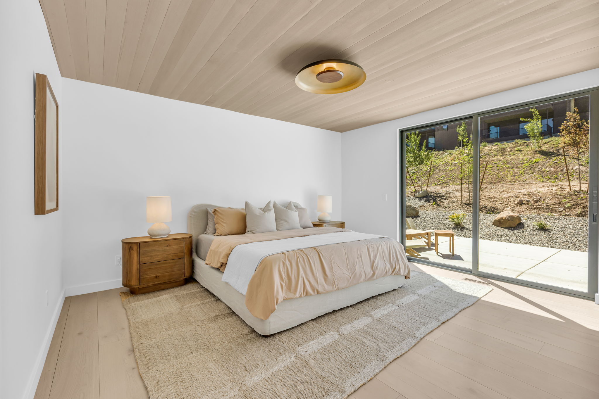 Spacious room featuring light wood-finish flooring, a full wall of sliding glass doors, a wood-paneled ceiling, and a modern flush-mount light fixture