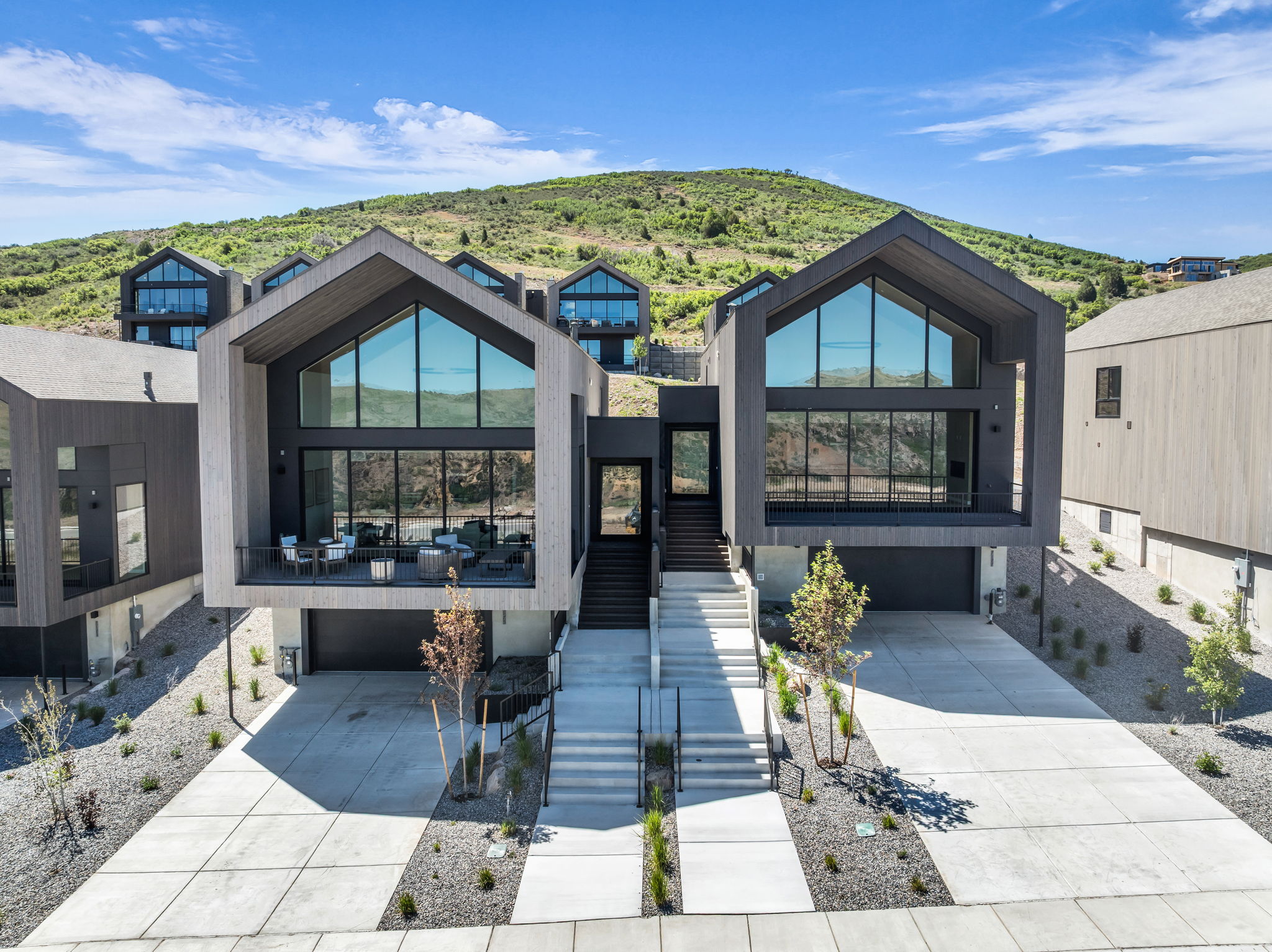 Modern architectural design featuring expansive glass facades, a covered balcony, integrated garage access, and a concrete driveway