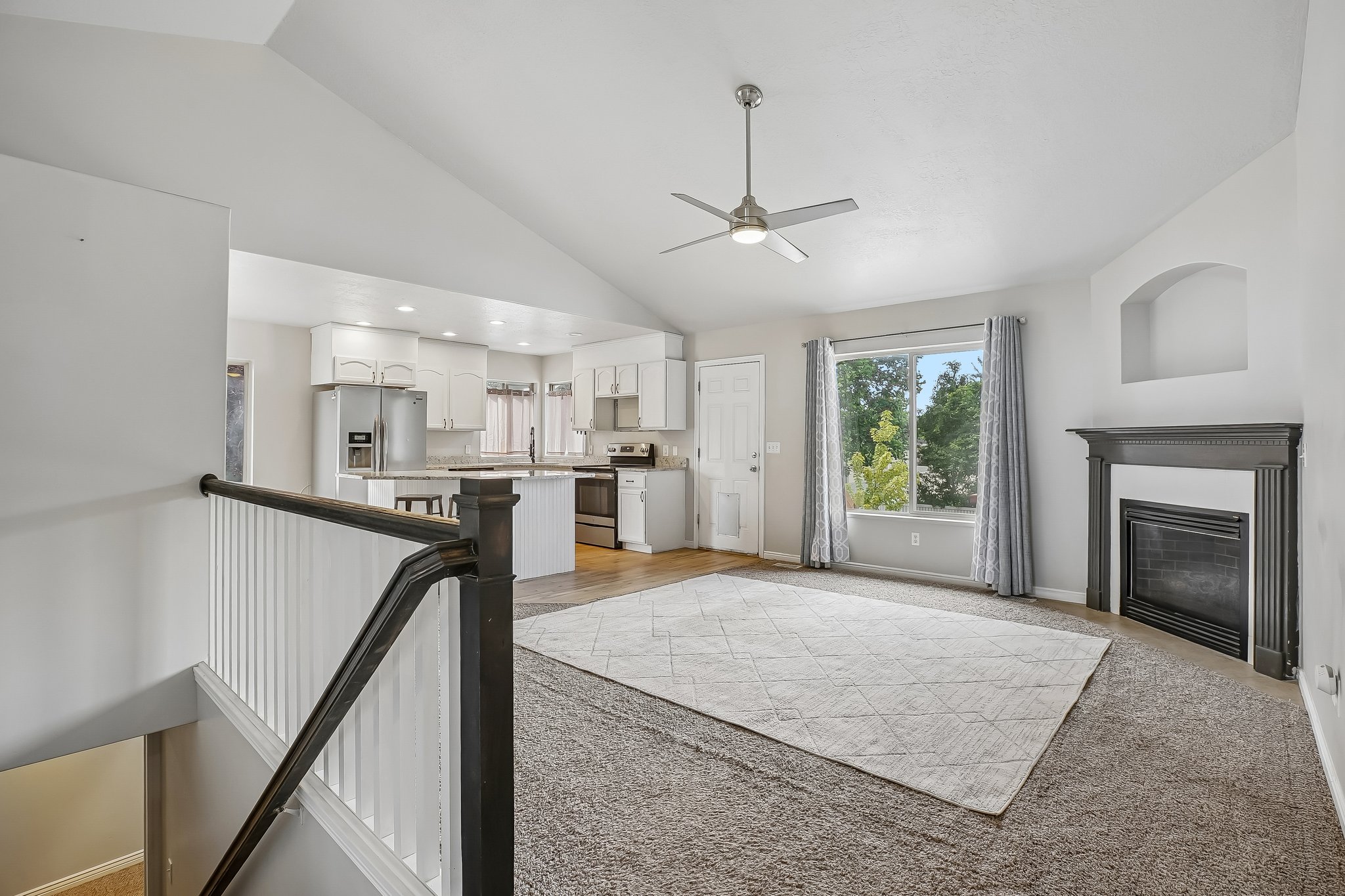 Open-concept living area featuring vaulted ceilings, a ceiling fan with integrated lighting, and a fireplace with a decorative mantel and hearth