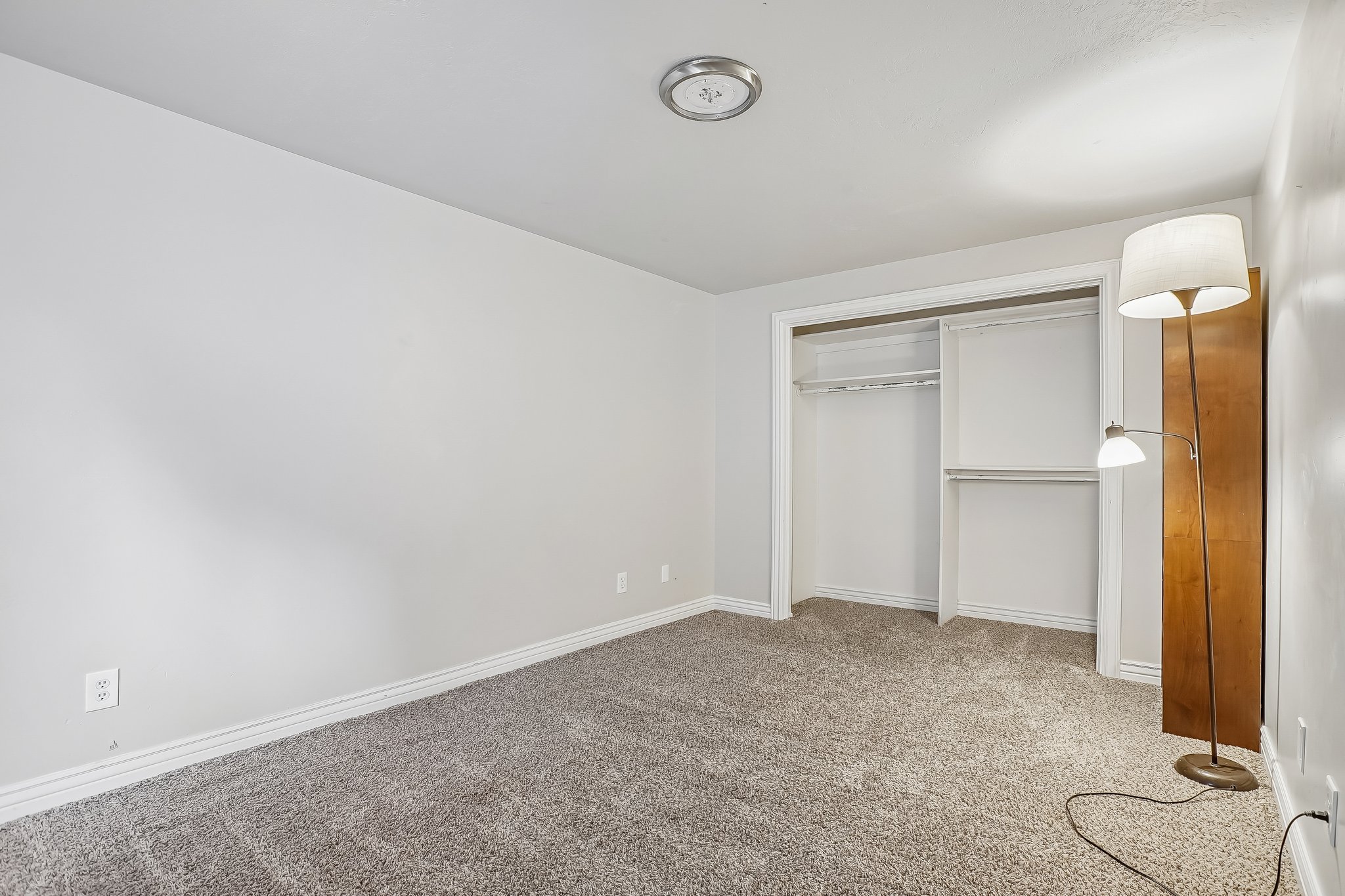 Room featuring light gray wall paint, gray carpet flooring, white baseboards, and a built-in closet with shelving and hanging rods
