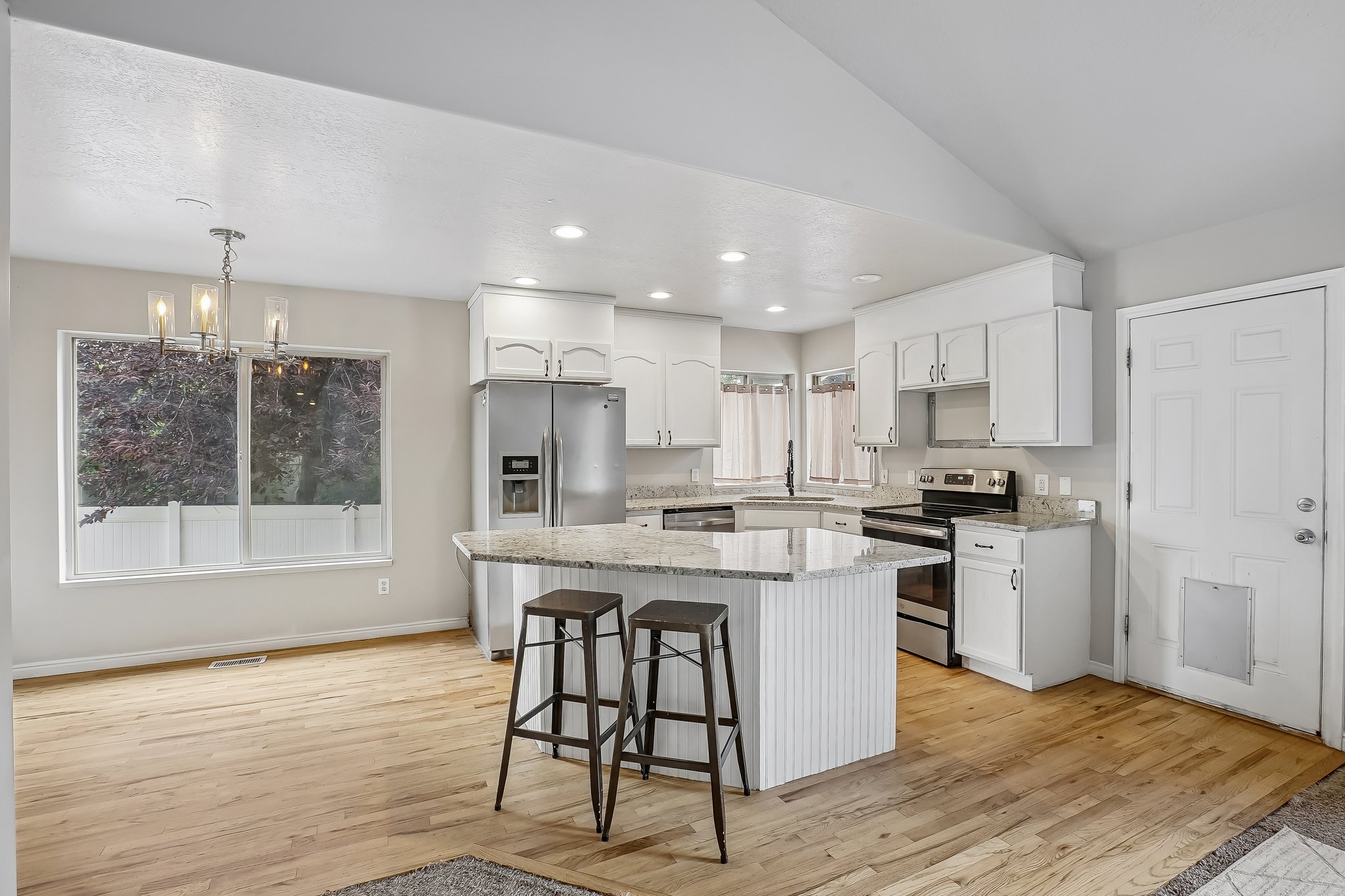 Open-concept kitchen and dining area featuring light wood-finish flooring, white cabinetry, granite countertops, and stainless steel appliances
