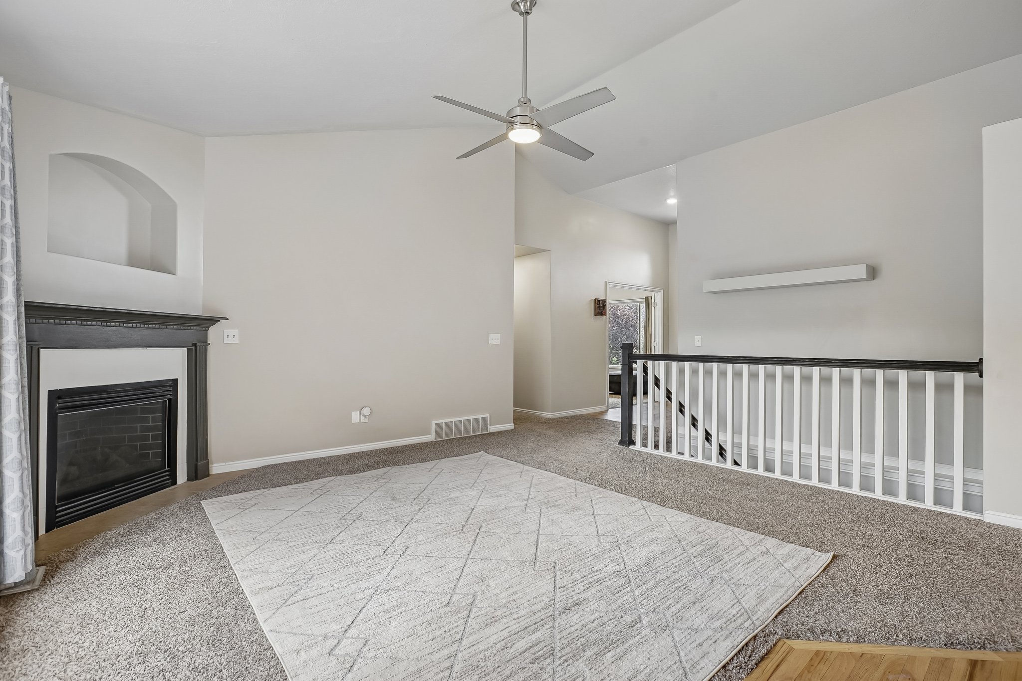 Spacious living area featuring vaulted ceilings, a fireplace with a dark mantel, and an arched wall niche