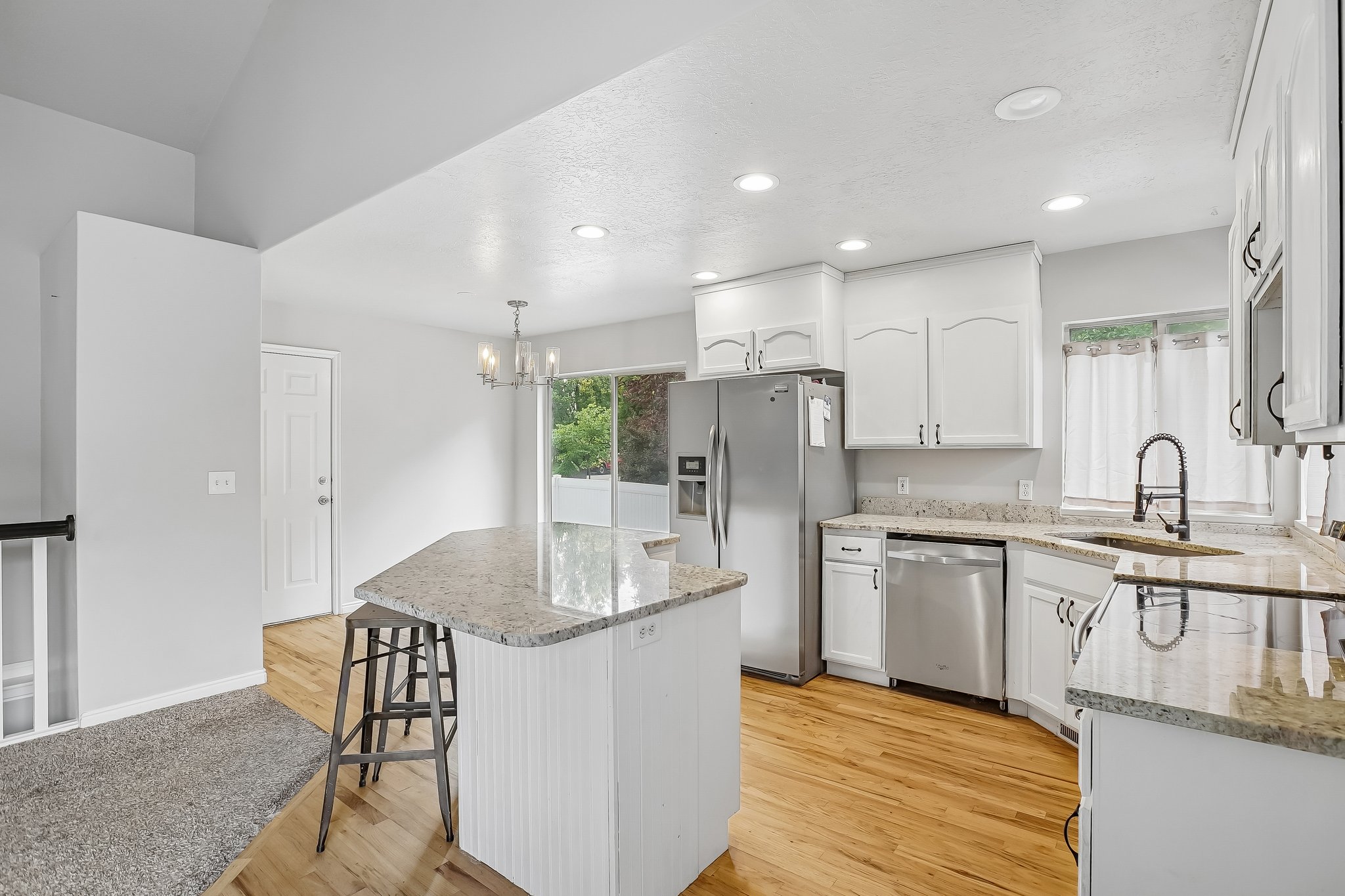 Bright kitchen featuring a central island with seating, white cabinetry, stainless steel appliances, and light-toned countertops