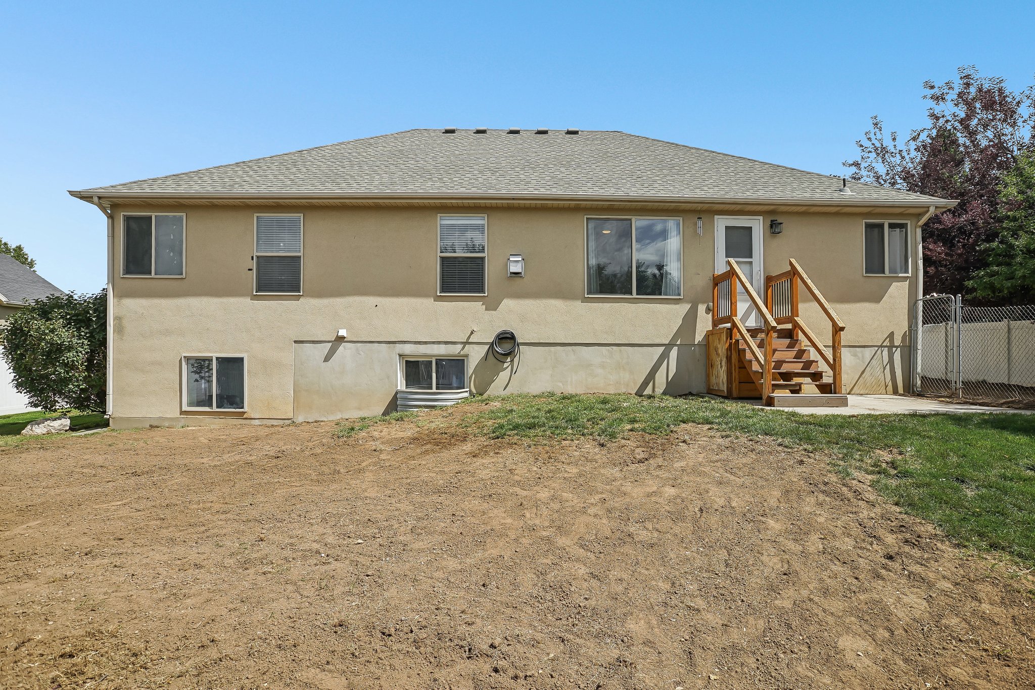 Rear exterior featuring stucco siding, a wood deck with stairs, a patio, and a sloped yard