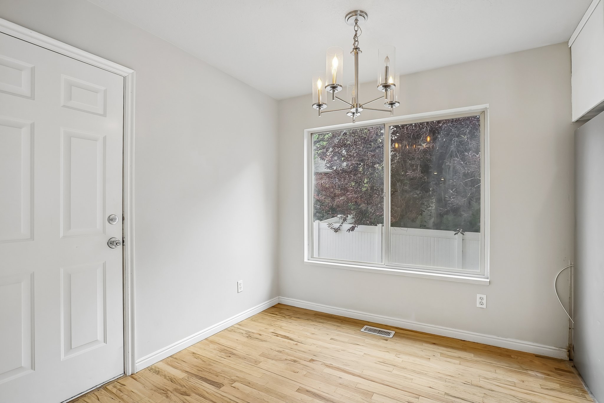 Open room featuring wood-finish flooring, a contemporary brushed nickel chandelier, and a large window