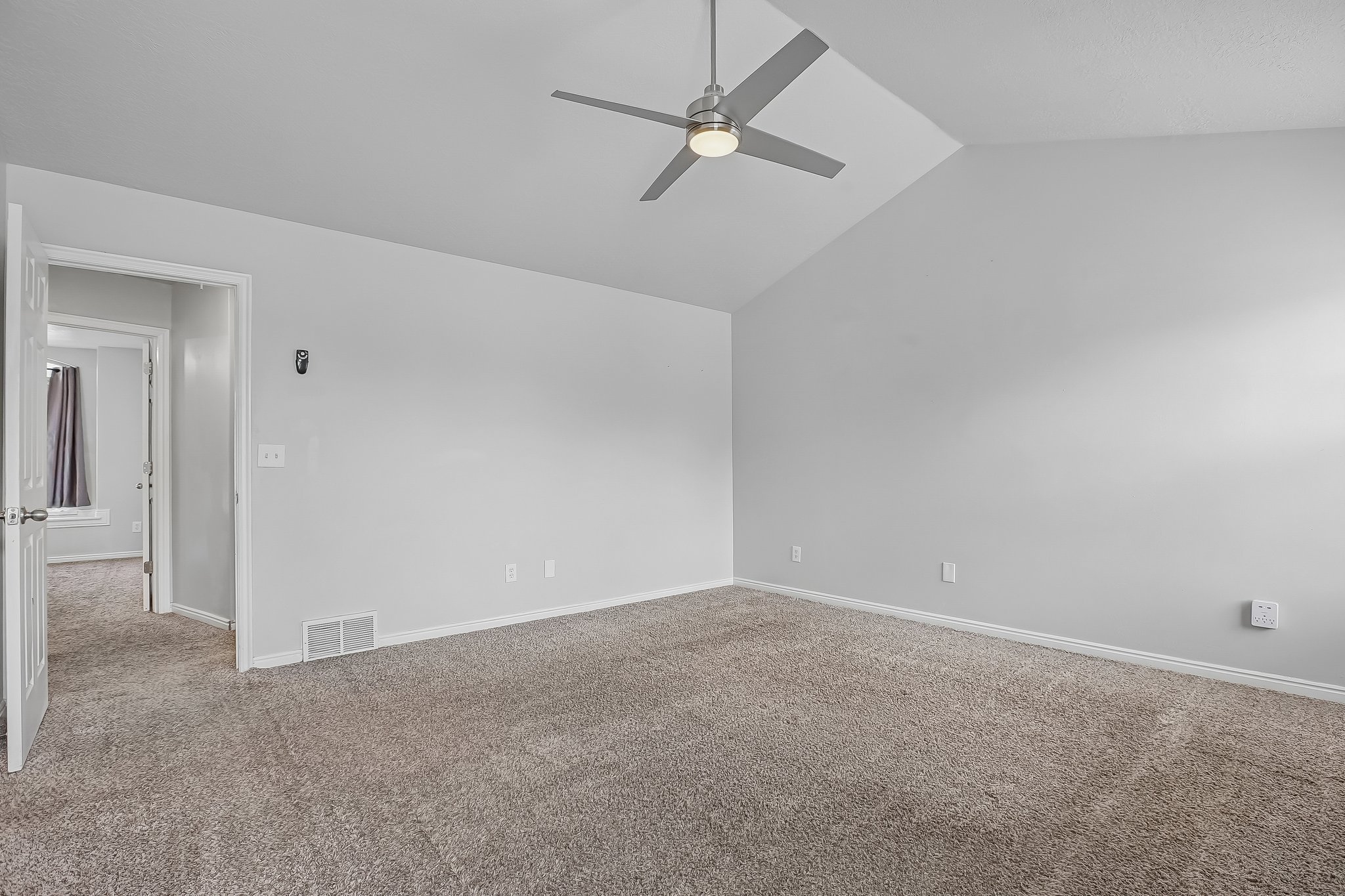 Spacious room featuring vaulted ceilings, a ceiling fan with integrated lighting, light gray wall paint, white trim, and plush carpet flooring