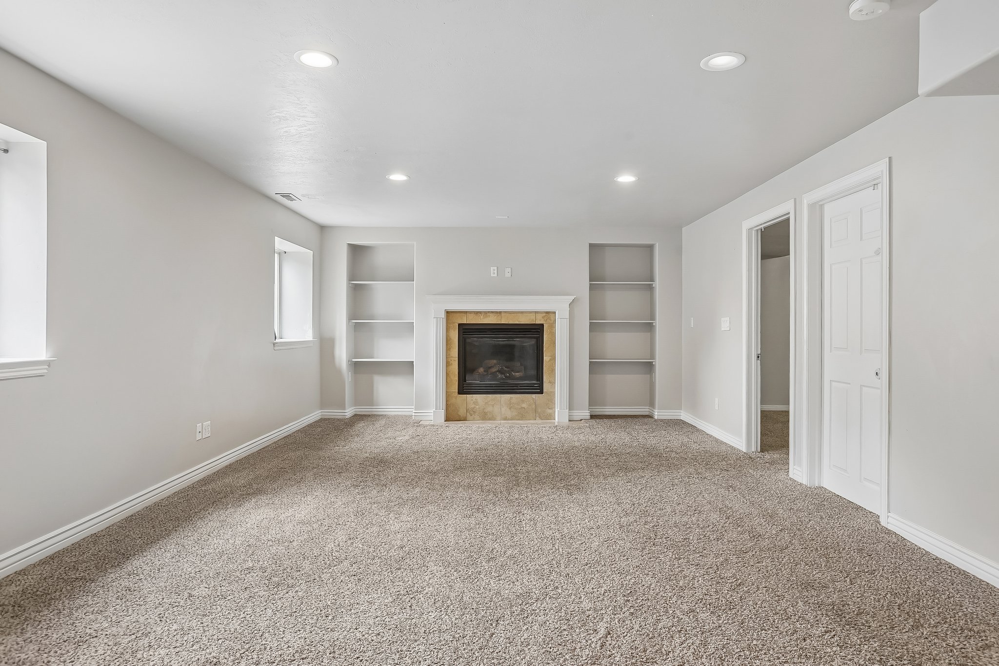 Spacious carpeted room featuring a fireplace with a stone surround and white mantel, flanked by built-in shelving