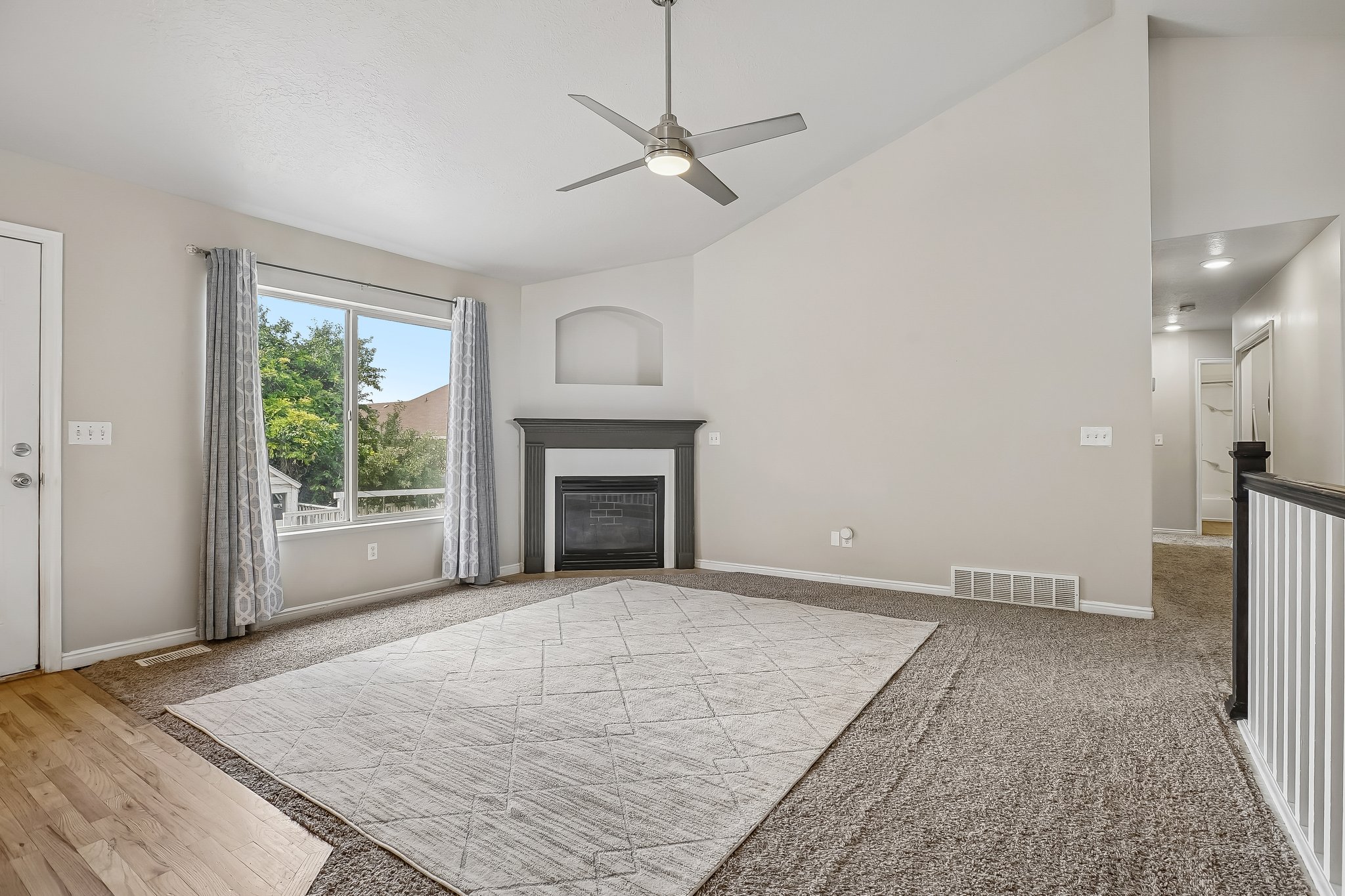 Open living space featuring a vaulted ceiling with a ceiling fan, a fireplace with a mantel, and a large window