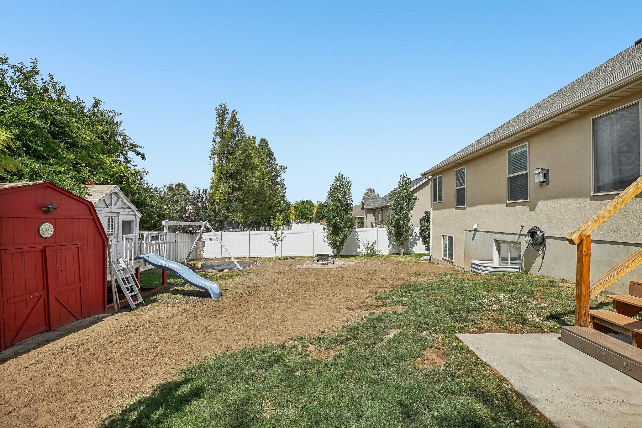 Private backyard space featuring a red storage shed, a white vinyl privacy fence, and a multi-level deck with wooden stairs