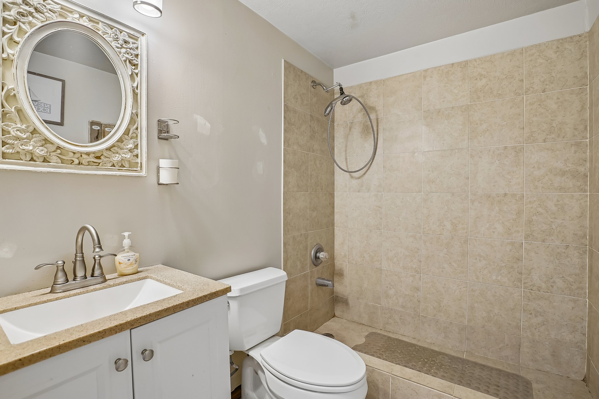 Bathroom featuring a tiled shower with a handheld showerhead, a white vanity with a light-colored countertop, and a decorative mirror