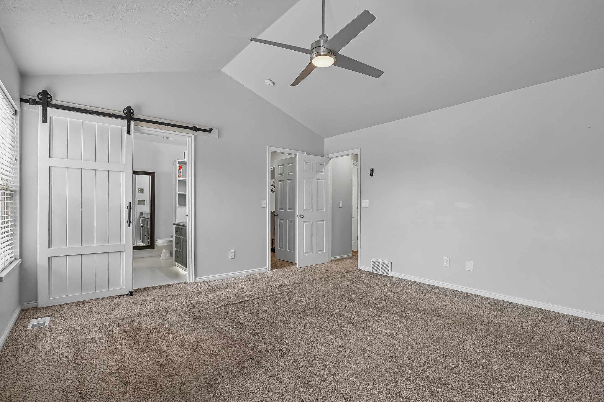 Vaulted ceiling room featuring a modern ceiling fan with integrated lighting, soft grey wall paint, and plush carpeting