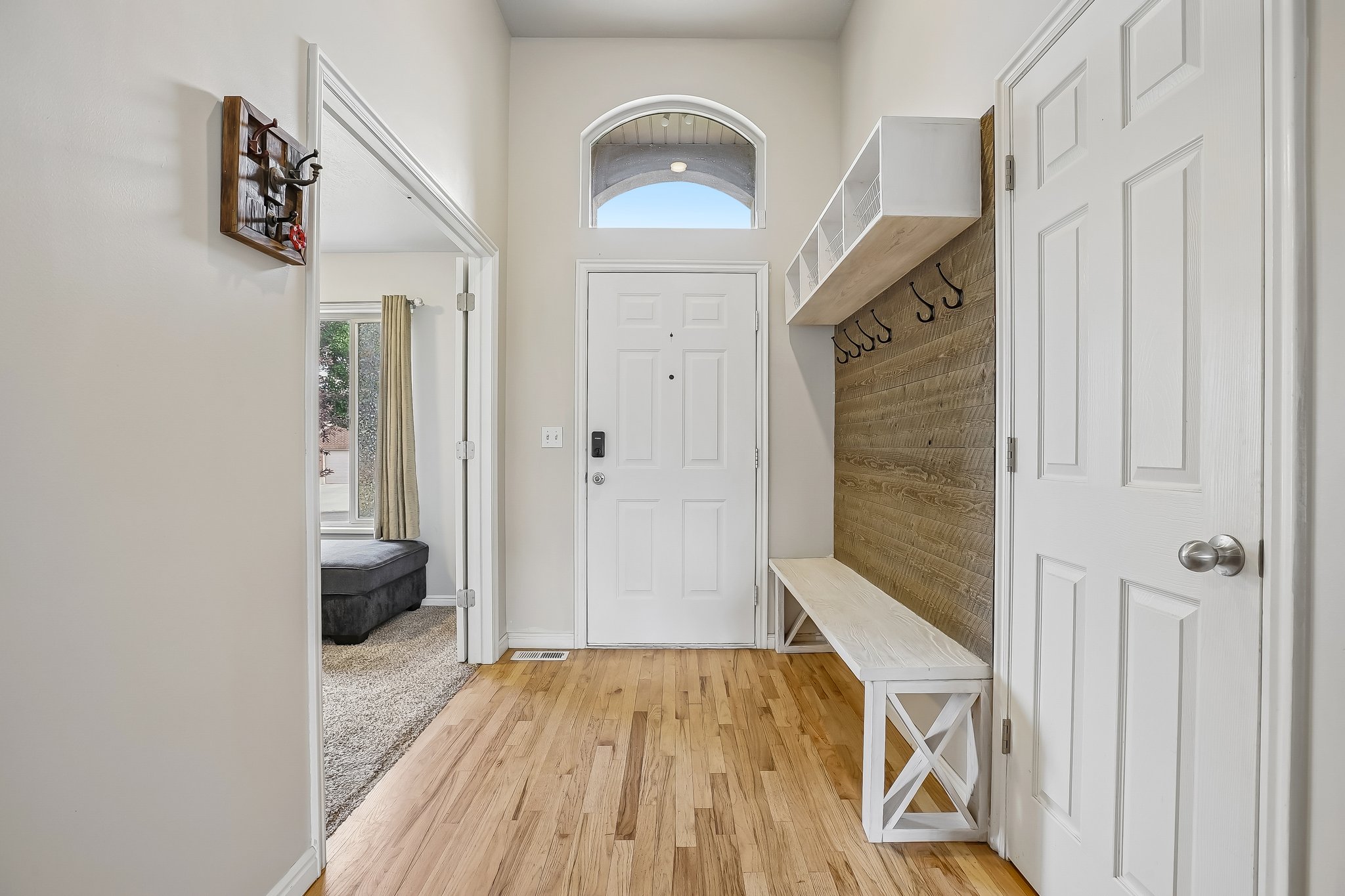Entryway featuring wood-finish flooring, a white paneled door with an arched transom window, a built-in bench with storage cubbies, and an accent wall with shiplap-style paneling