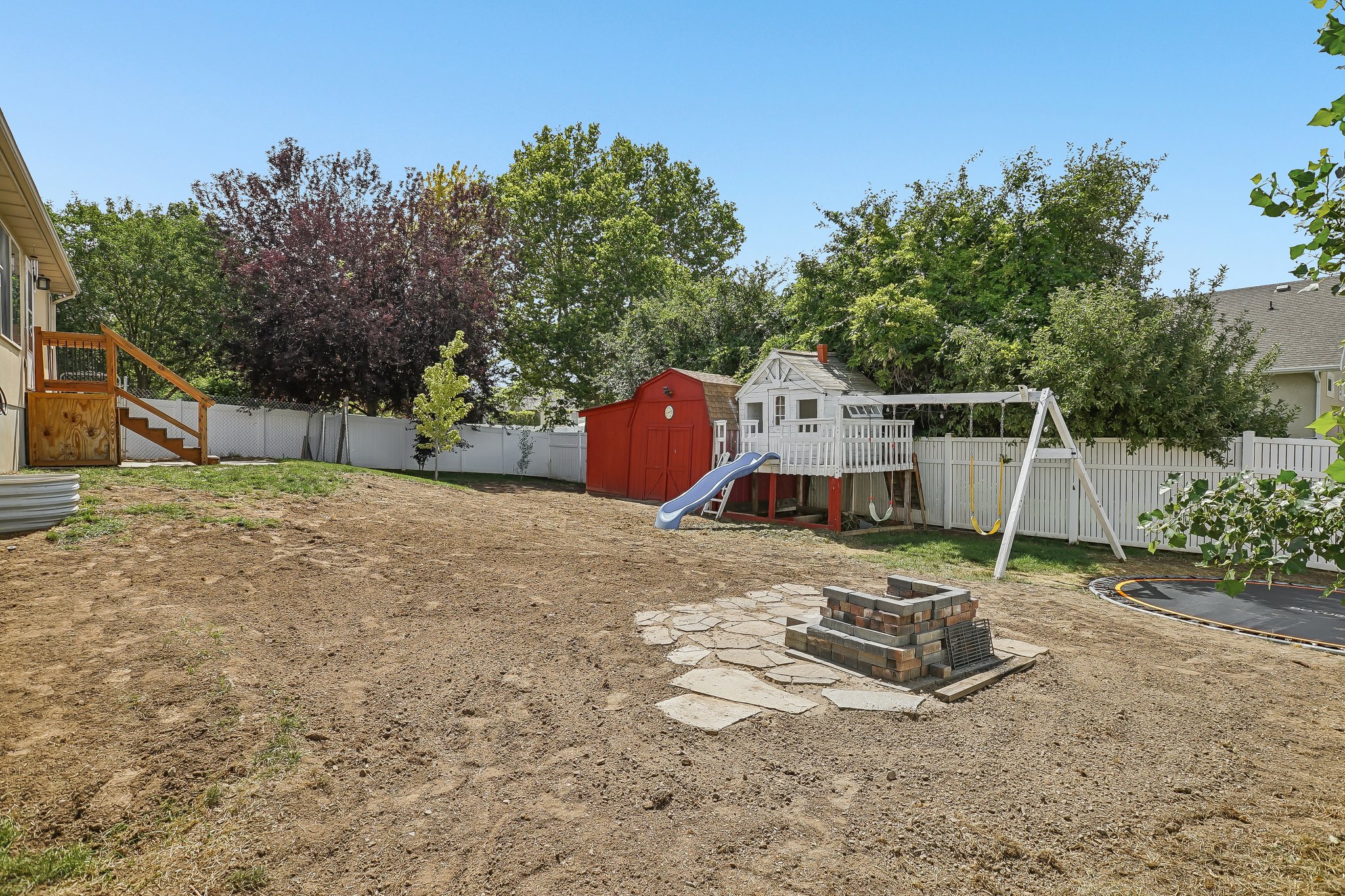 Spacious backyard featuring a brick fire pit on flagstone, a tiered deck with stairs, and a white picket fence