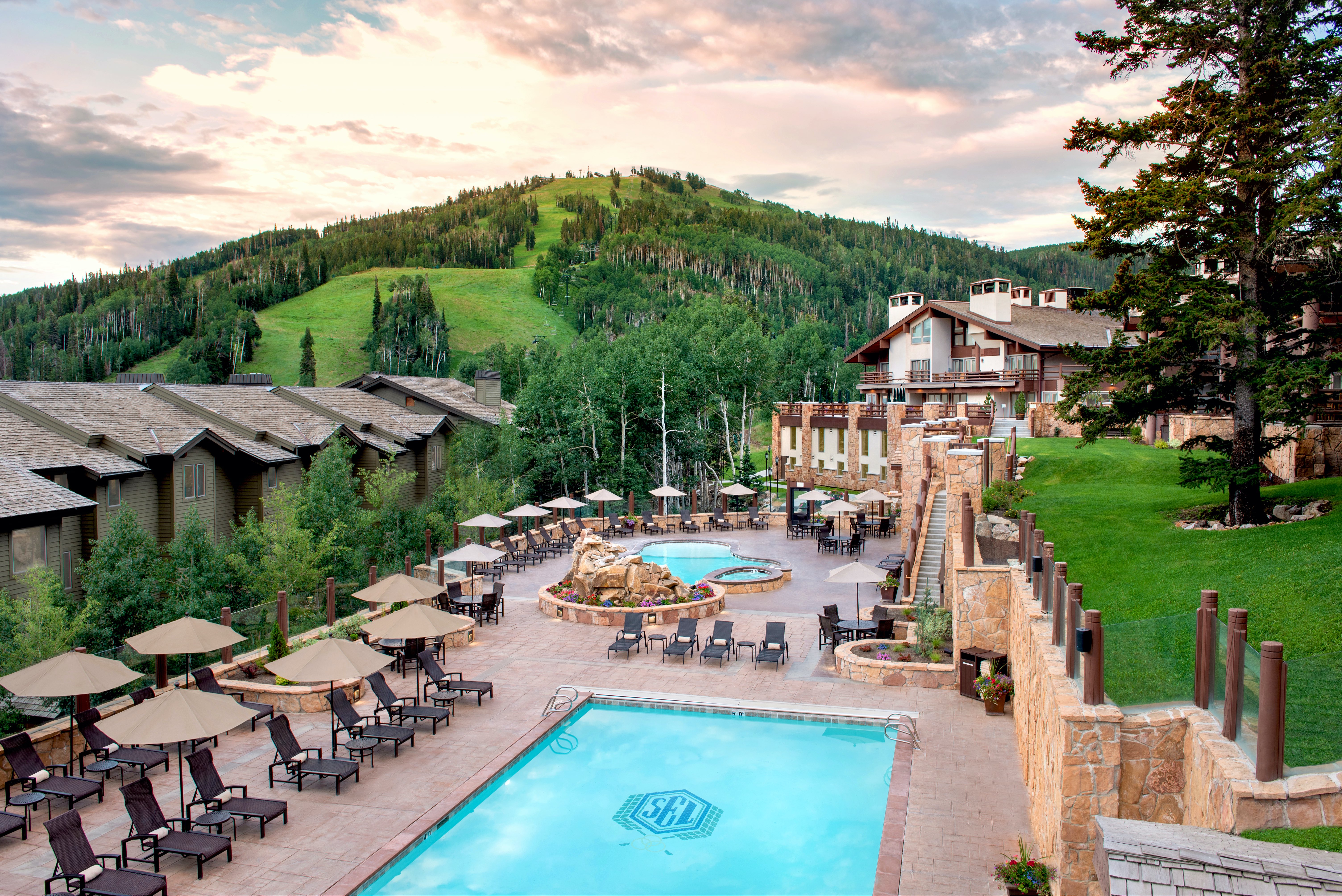 Expansive outdoor amenity space featuring a large swimming pool, a separate hot tub, and multiple lounge areas with umbrellas