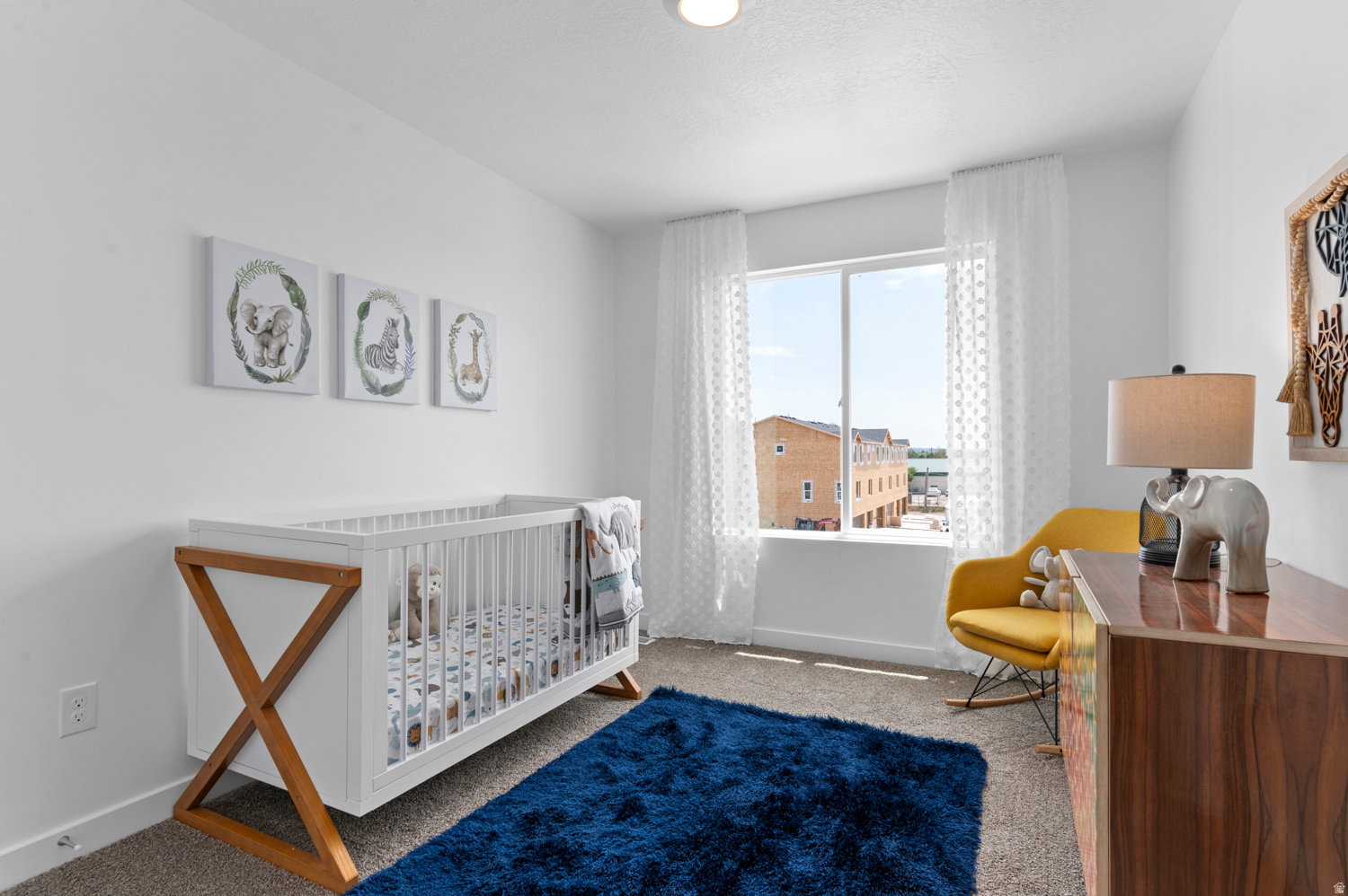 Bright room featuring a large window with white sheer curtains, neutral carpet flooring, and white walls