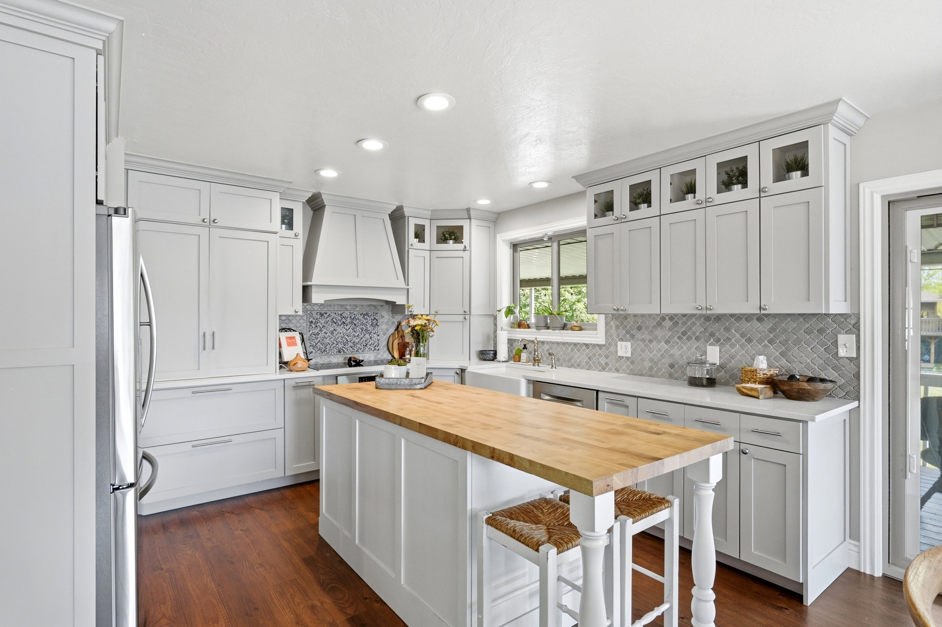 Kitchen featuring a central island with a wood-finish countertop, light gray cabinetry, stainless steel appliances, a gray tiled backsplash, and recessed lighting