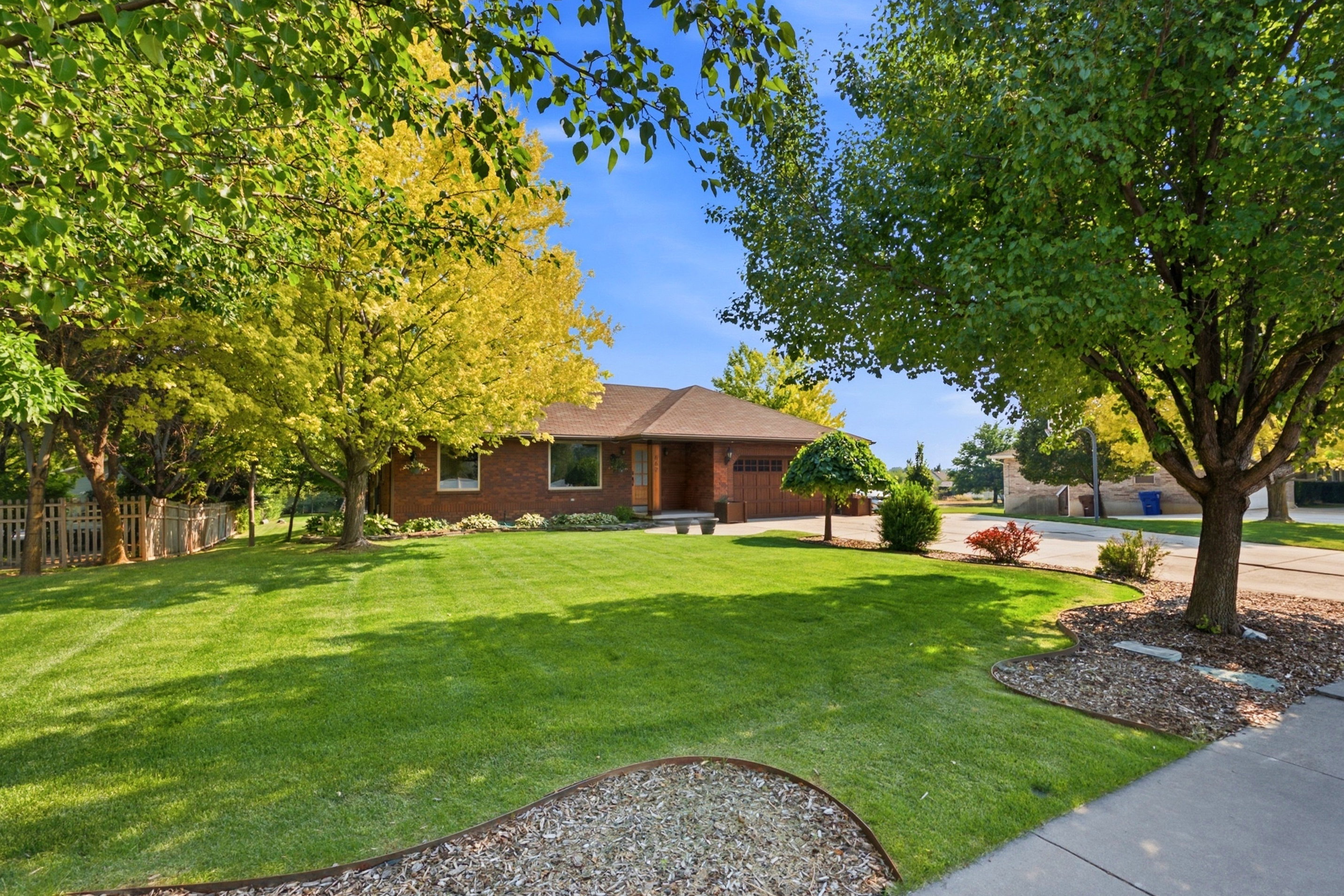 Brick exterior residence featuring a brown shingle roof, mature trees, an expansive lawn, and foundation plantings