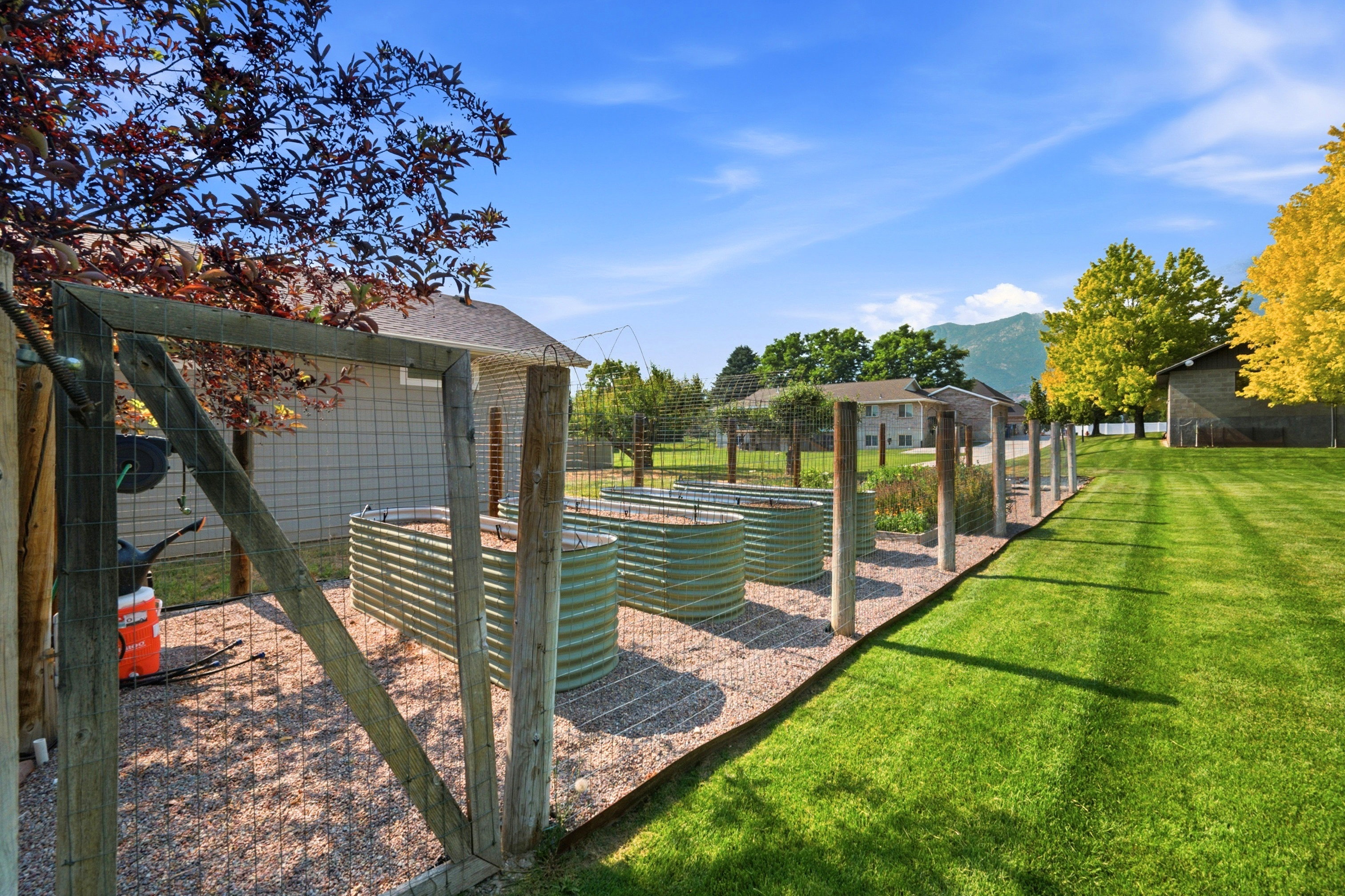 Expansive backyard featuring a manicured lawn, established garden beds, a gravel-covered garden area, a wire fence, and mature trees