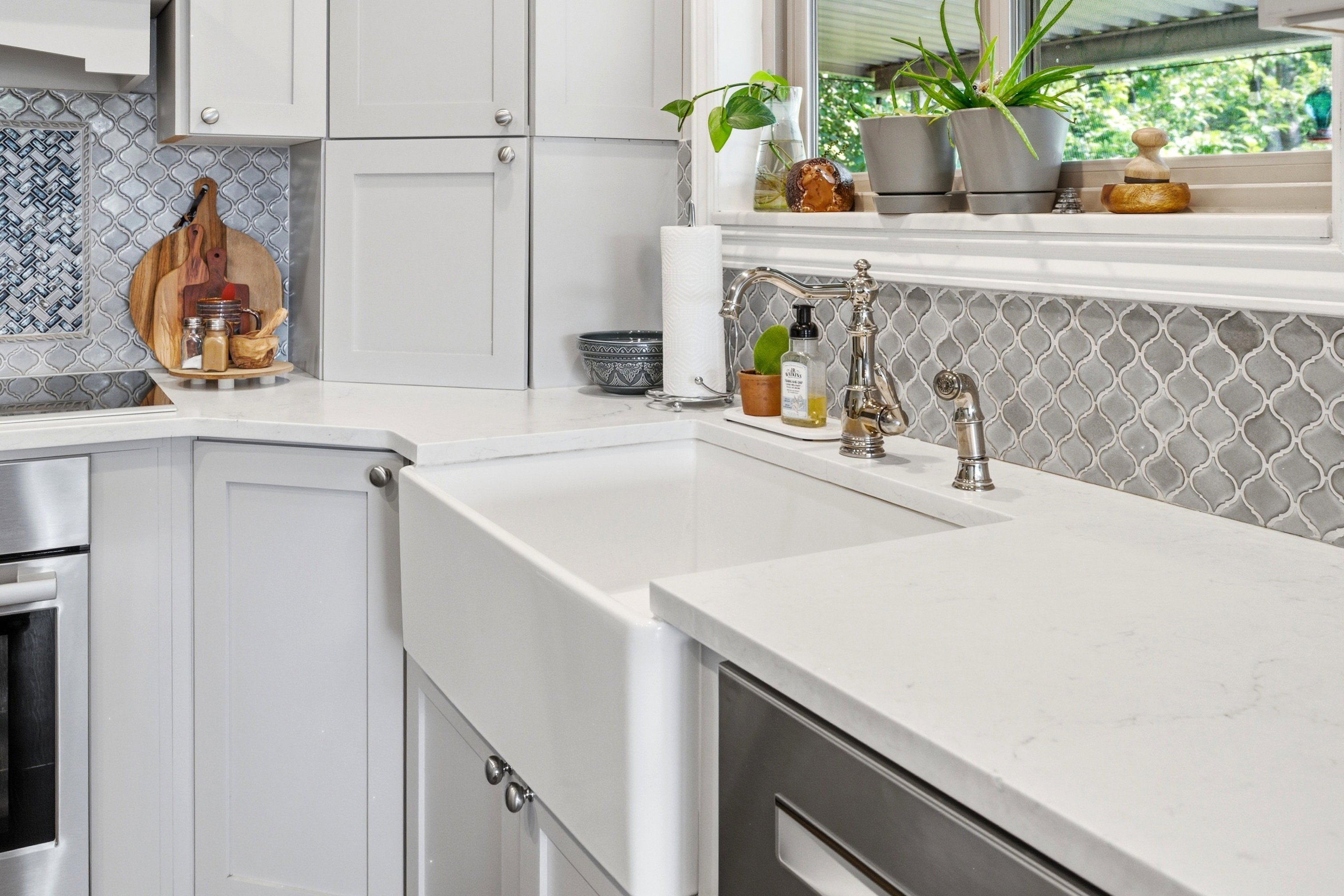 White apron-front sink paired with polished chrome faucet and sprayer, set within white countertops