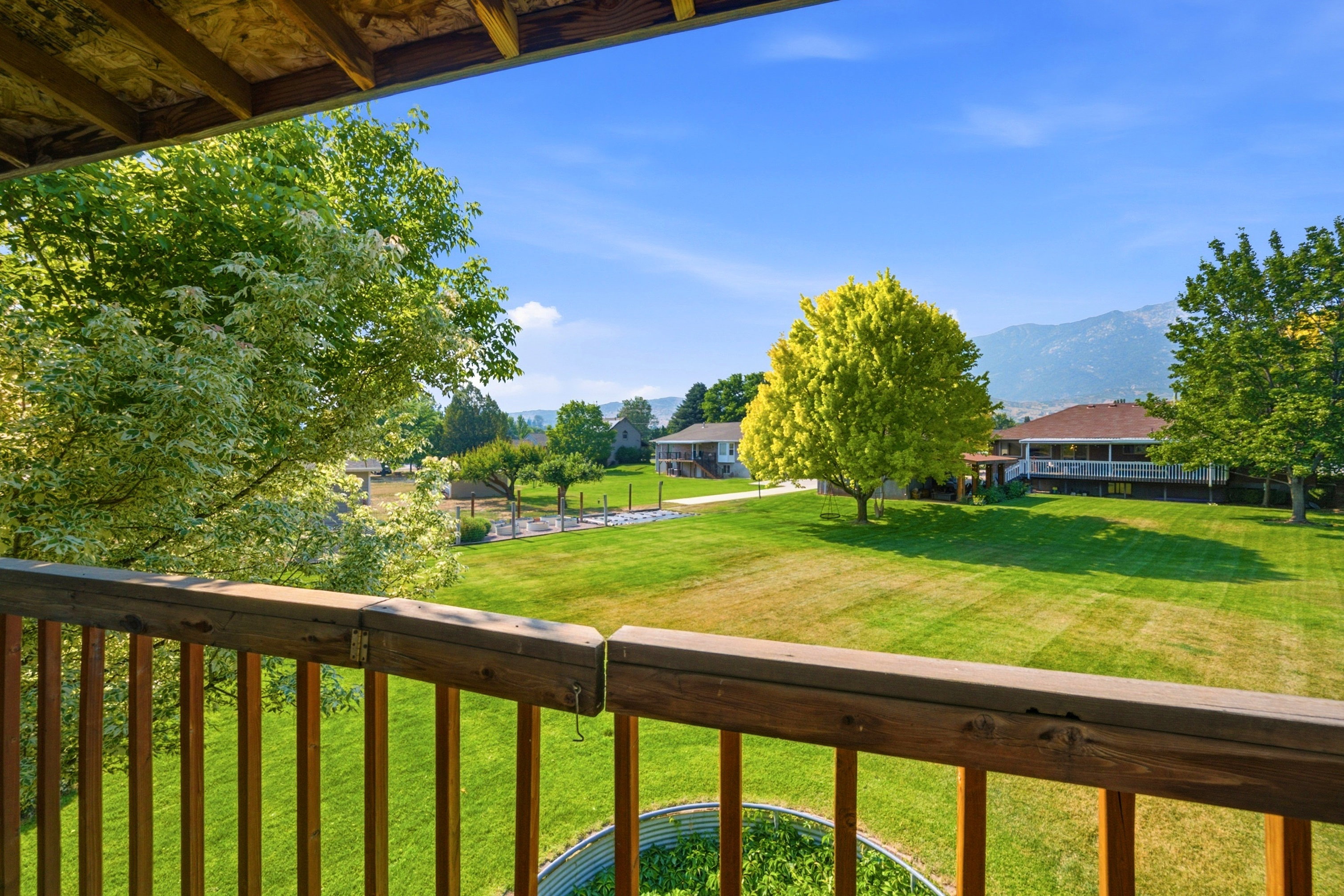 Expansive green space featuring a vast lawn, mature trees, mountain backdrop, and a private balcony with wood railing