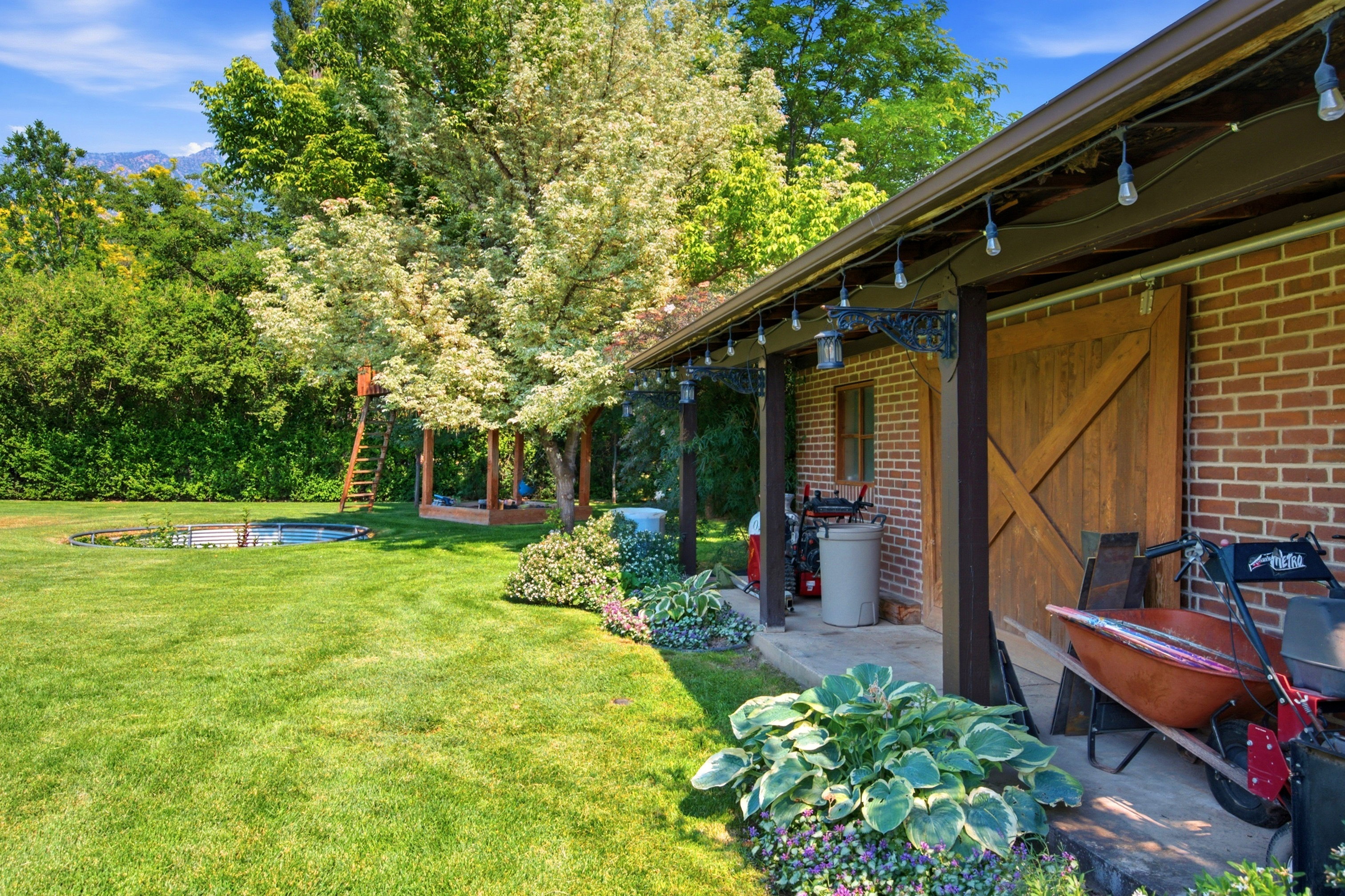 Expansive green lawn featuring a built-in trampoline, mature trees, and a wooden play structure