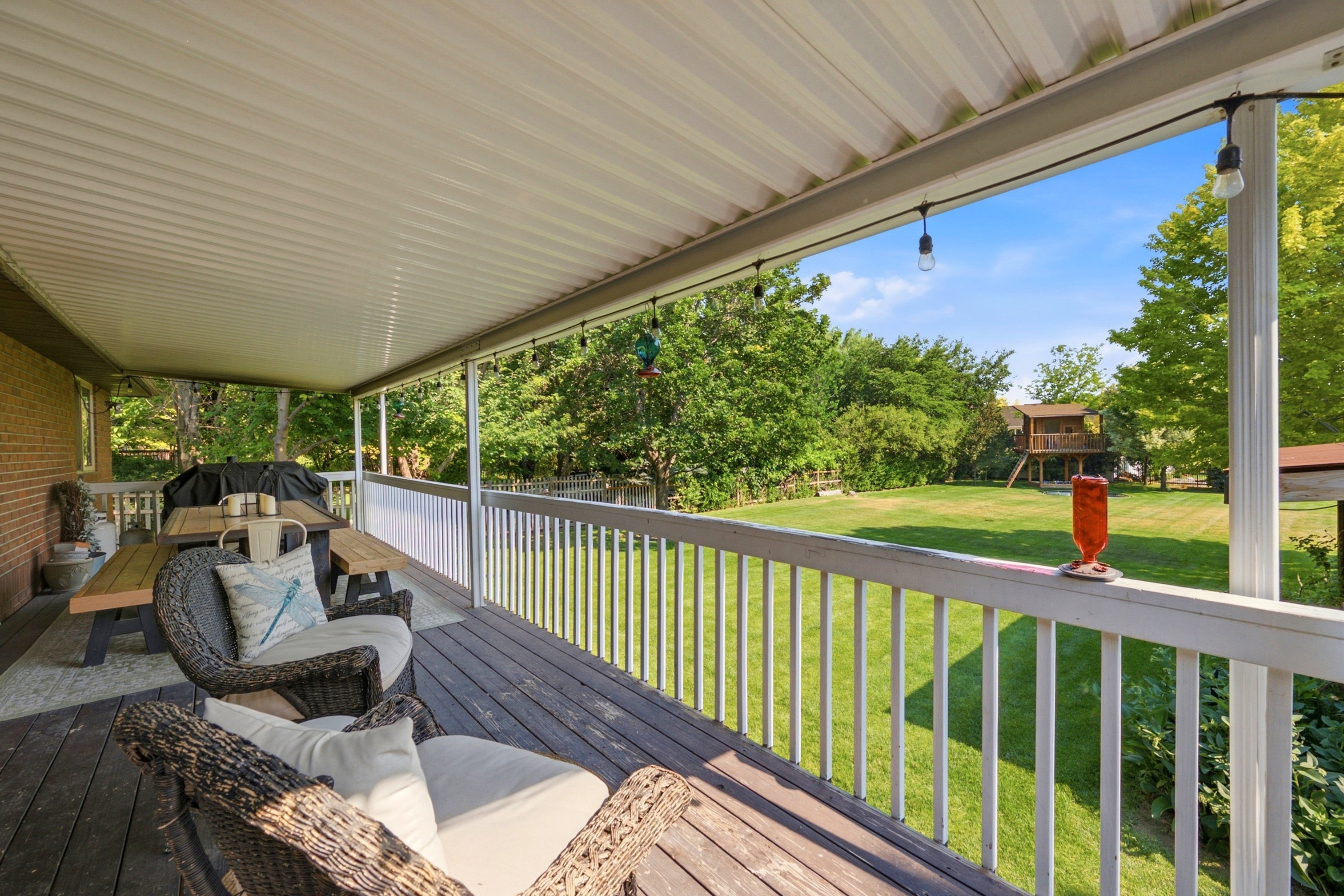Spacious covered wood-finish deck with white railing and string lighting