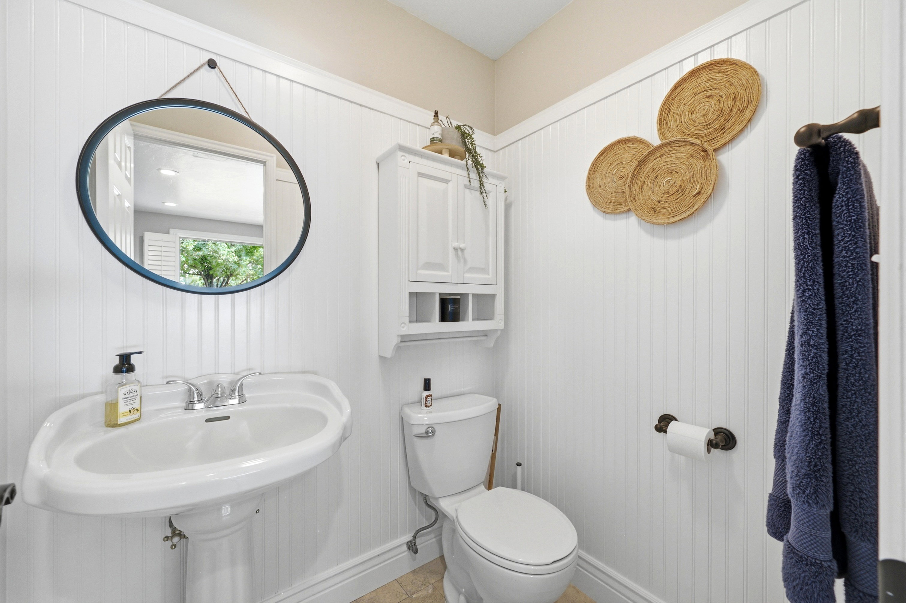 Bathroom featuring a pedestal sink, wall-mounted mirror, beadboard paneling, and a wall cabinet with open shelving