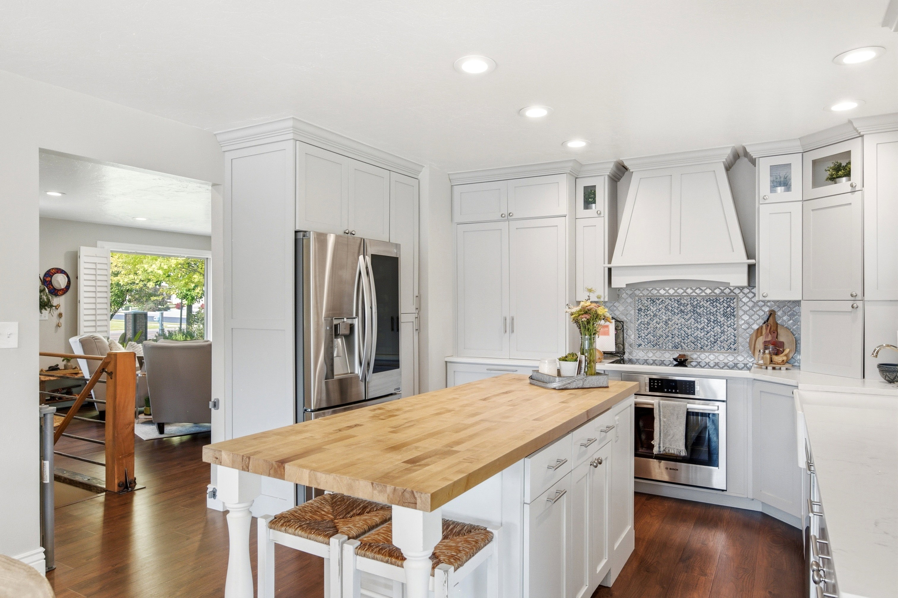 Kitchen featuring a large wood-top island with seating, stainless steel appliances, custom cabinetry, and a geometric tile backsplash