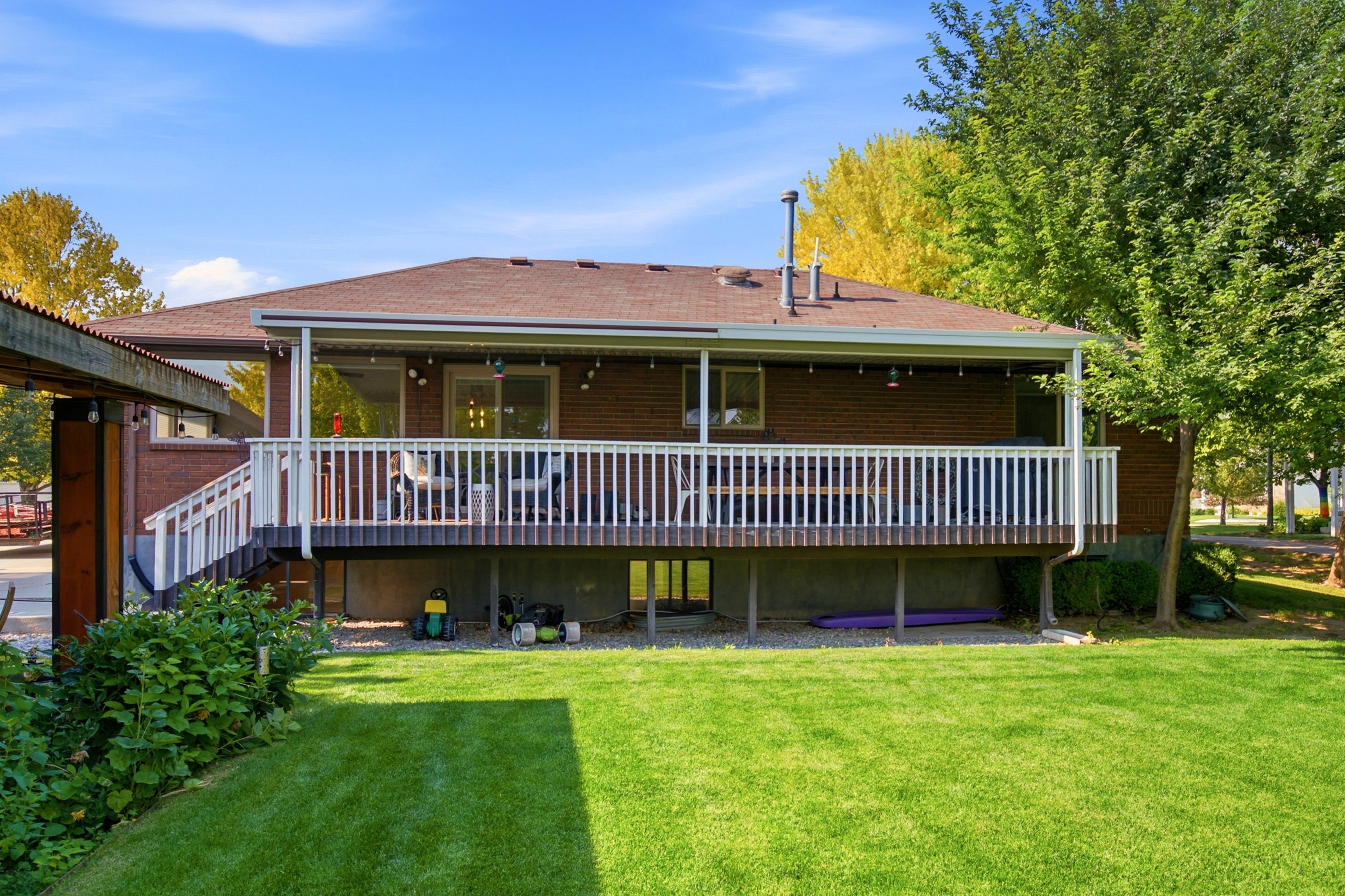 Expansive backyard featuring a manicured lawn and mature trees, complemented by a large elevated deck with white railings
