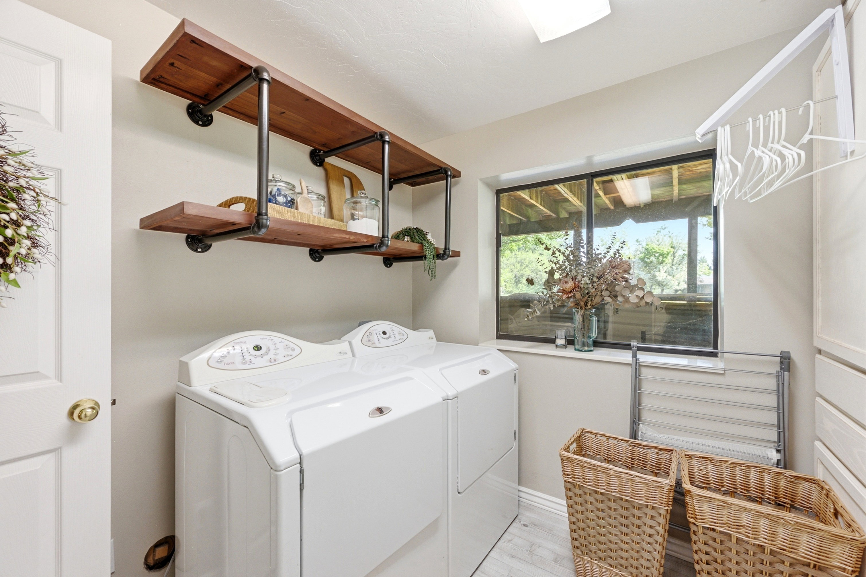 Dedicated laundry area featuring a window, wood-finish flooring, built-in shelving with industrial-style supports, and recessed ceiling lighting