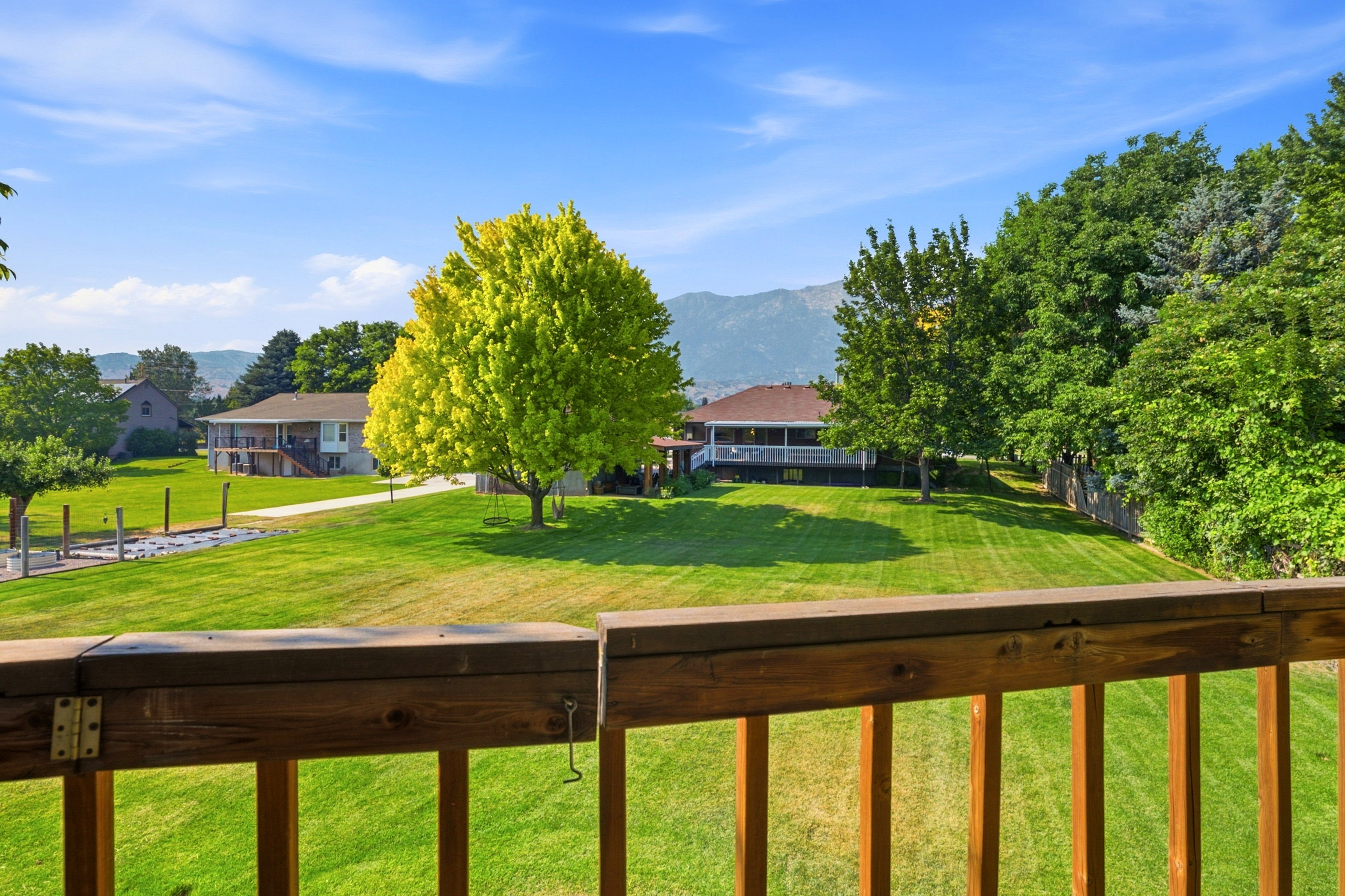 Expansive green lawn with mature trees and a distant mountain backdrop, framed by a wooden deck railing