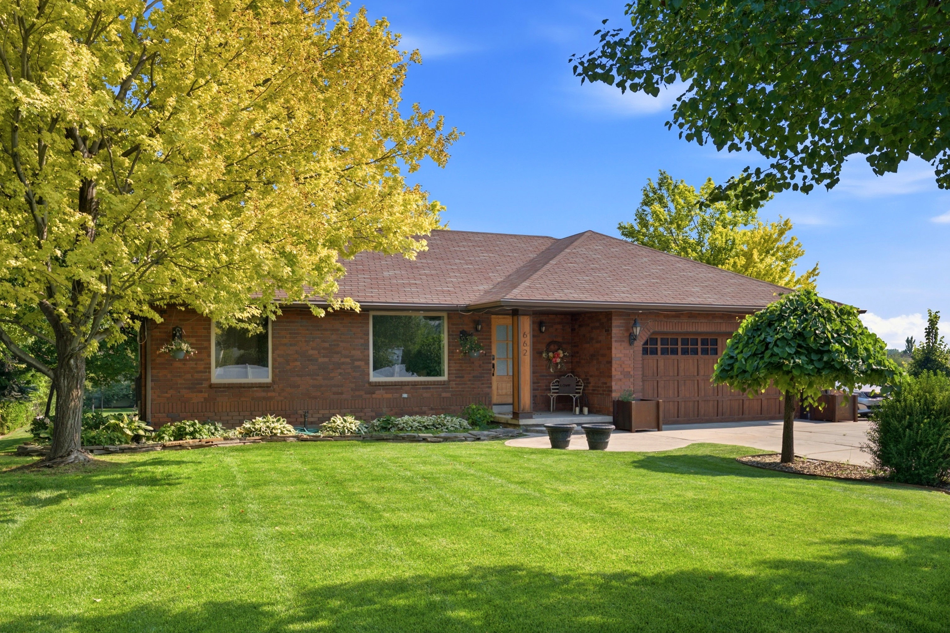 Brick facade ranch-style home featuring a brown asphalt shingle roof, attached two-car garage with a wood-look door, and a concrete driveway