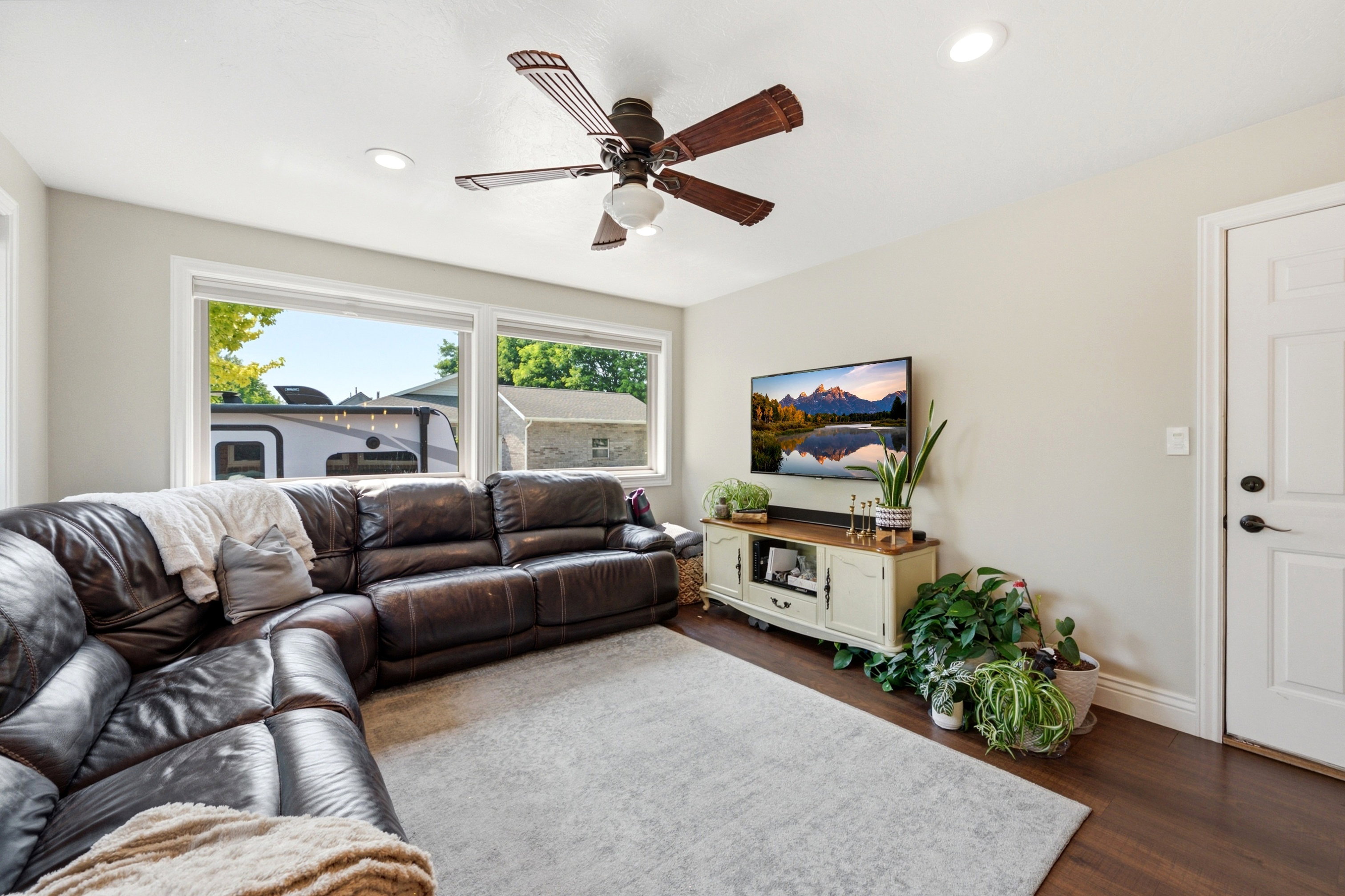 Spacious room featuring multiple large windows, recessed ceiling lighting, a ceiling fan with wood-finish blades, dark wood-finish flooring, and a white panel door