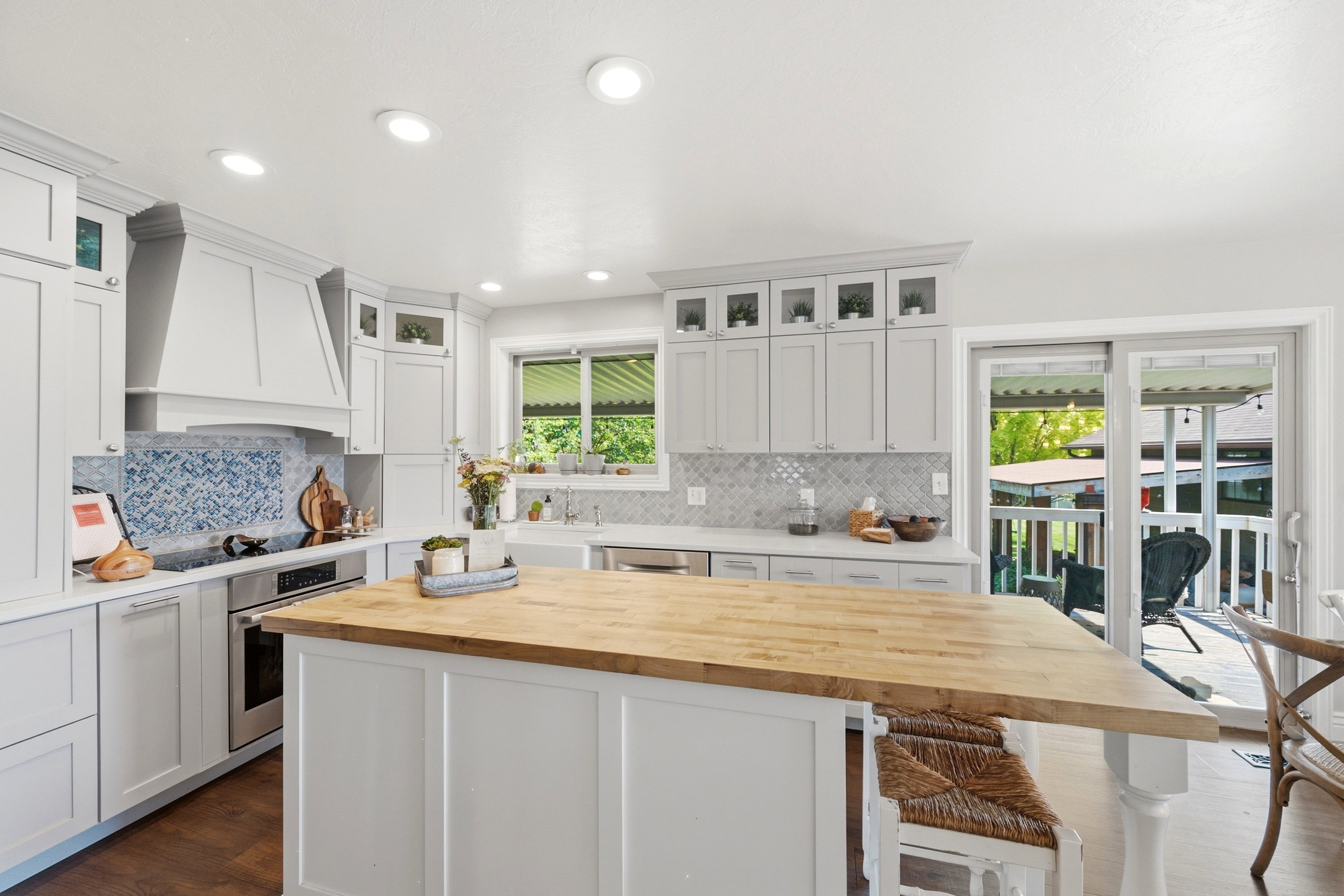 Kitchen featuring a substantial island with a butcher block countertop, white shaker cabinetry, white countertops, a patterned tile backsplash, and stainless steel appliances