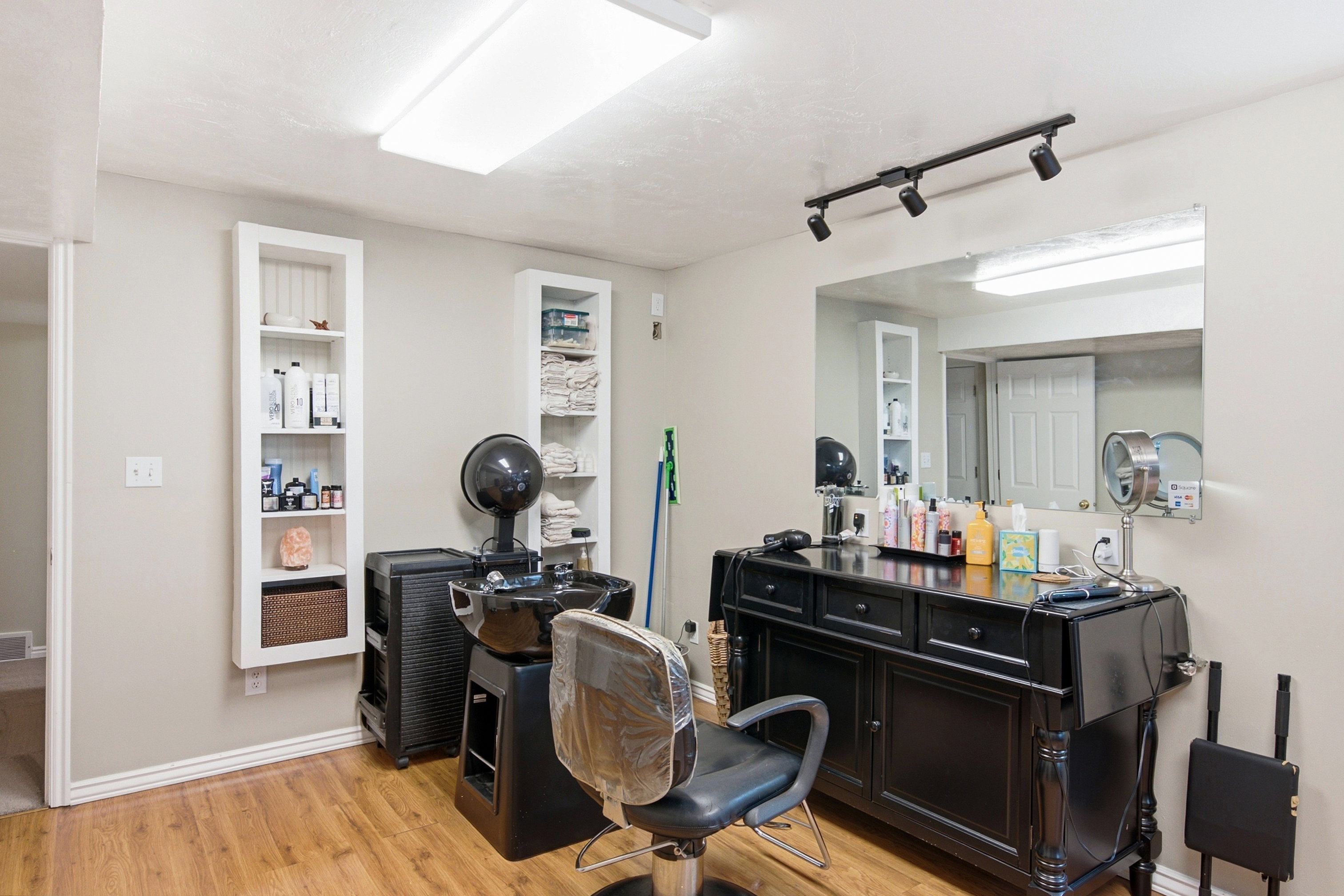 Room featuring wood-finish flooring, two built-in shelving units, a large wall-mounted mirror, and track lighting