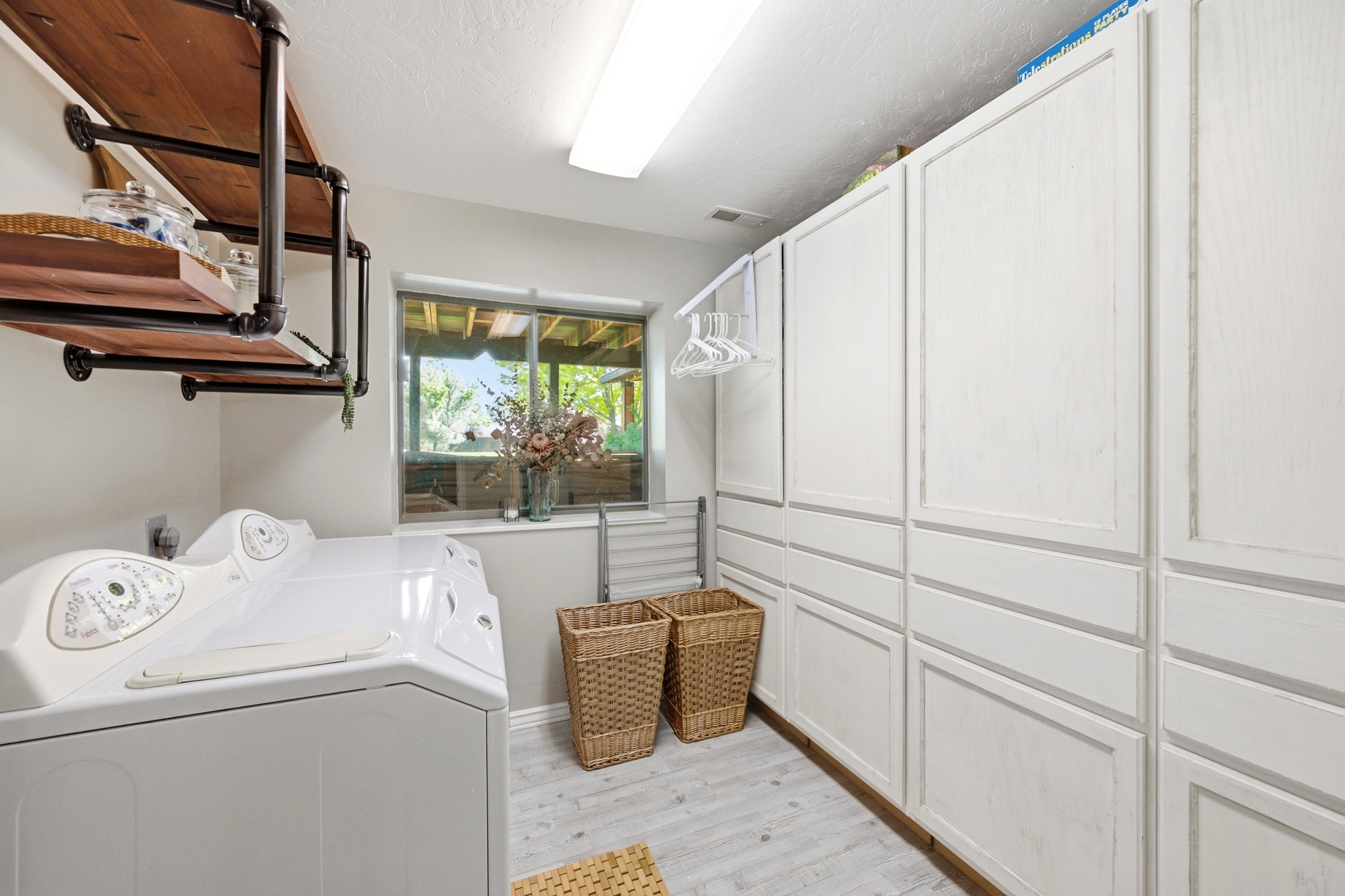 Laundry room featuring extensive white built-in cabinetry, wood-finish flooring, and a window providing natural light