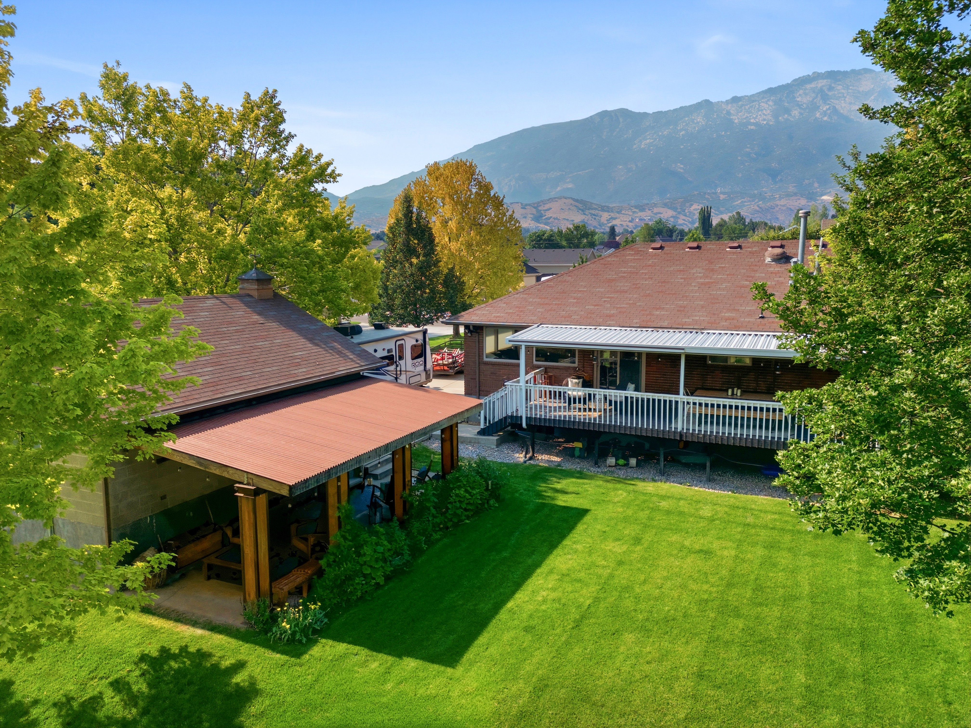 Expansive green lawn with a covered patio area featuring wood columns and a separate elevated deck