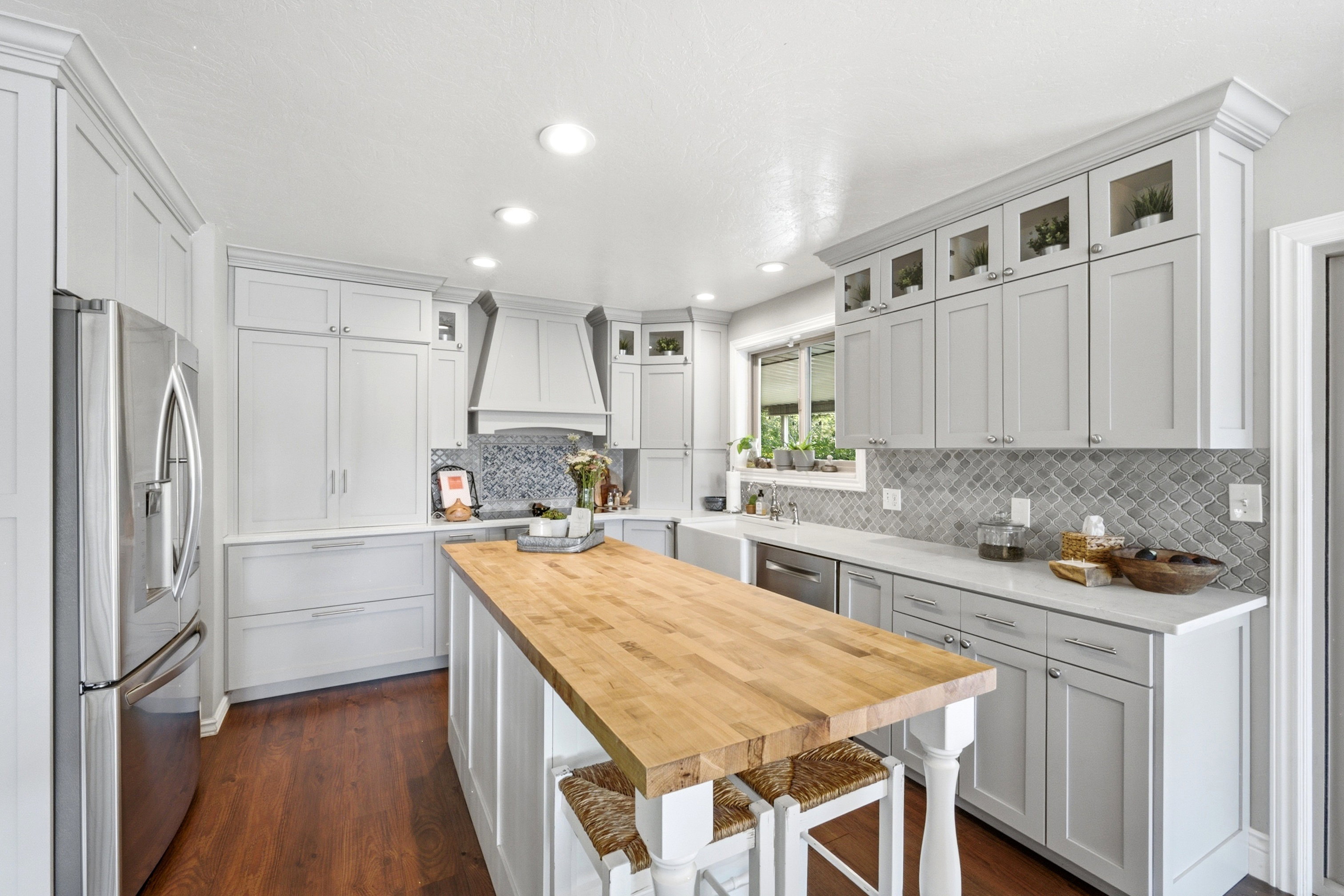 Modern kitchen featuring a wood-finish floor, white shaker cabinetry, stainless steel appliances, and an expansive butcher block island