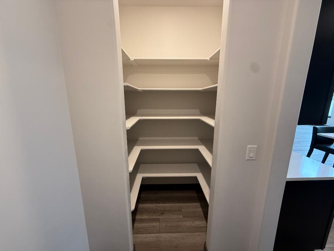 Spacious pantry featuring multiple tiers of shelving, L-shaped shelving, interior lighting, and wood-finish flooring