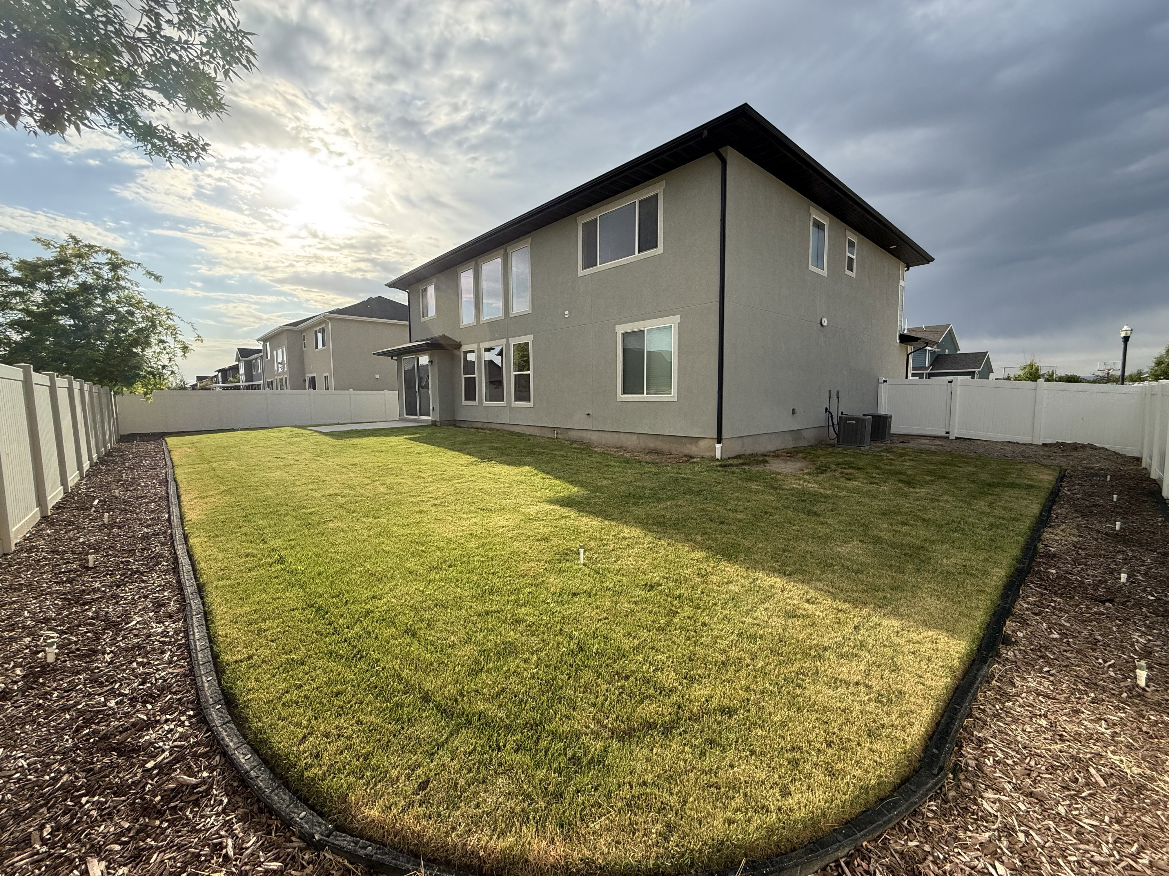 Fenced backyard featuring a manicured lawn, mulched borders, and a stucco exterior