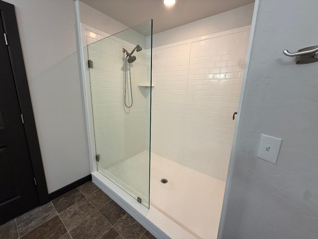 Glass-enclosed master walk-in shower featuring a white cultured surround, a built-in shelf, and a multi-function shower head