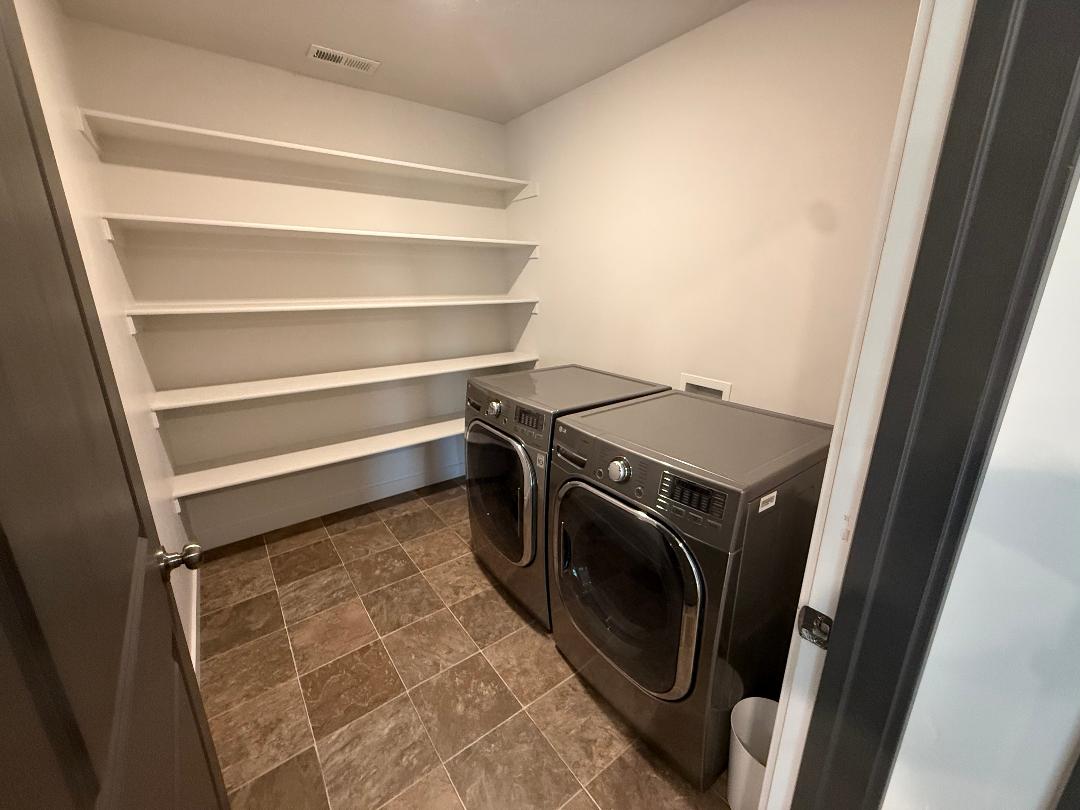 Dedicated utility space featuring extensive built-in shelving, tile flooring, and overhead lighting