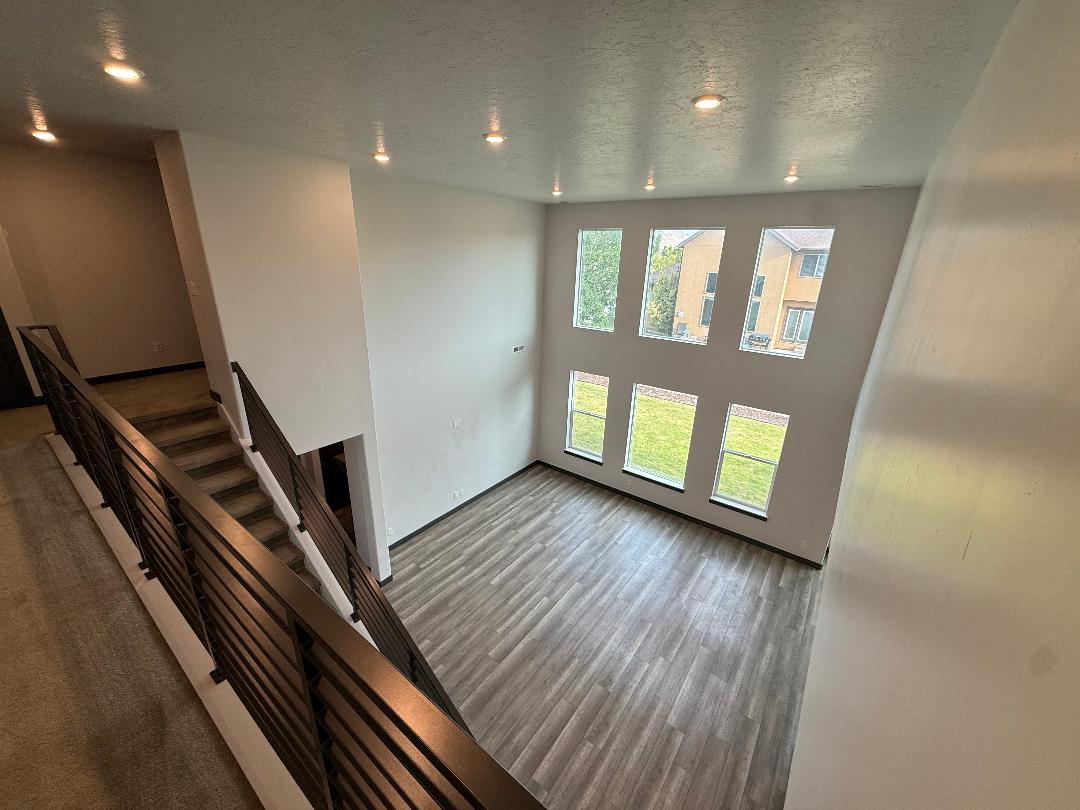 Two-story open concept living area featuring wood-finish flooring, a contemporary horizontal slat railing staircase, and a double-height window arrangement providing ample natural light