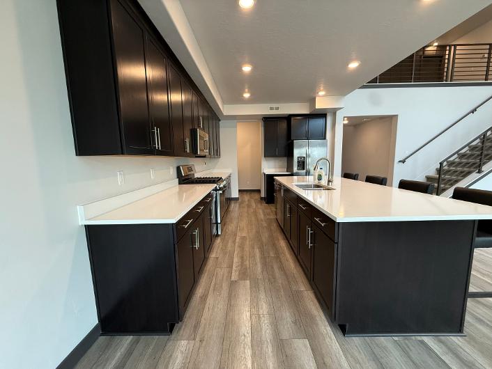 Open-concept kitchen featuring dark wood cabinetry, light countertops, stainless steel appliances, and wood-finish flooring