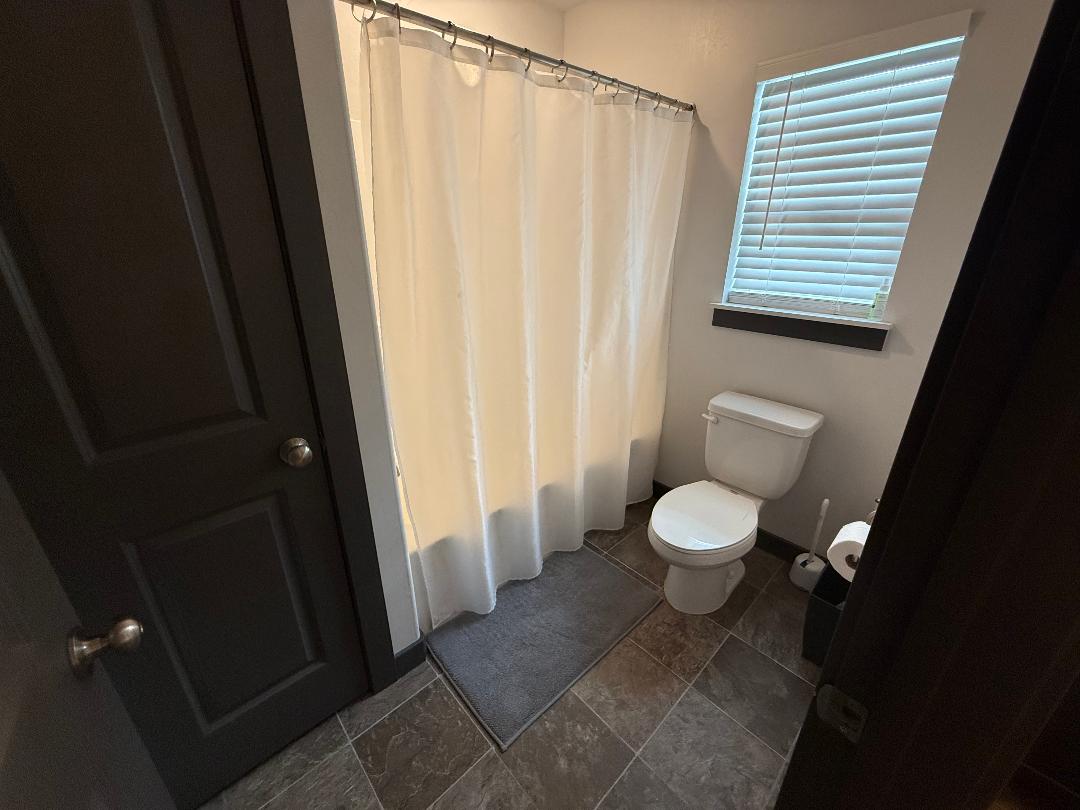 Bathroom featuring a shower with a white curtain, a white toilet, and dark-toned square tile flooring