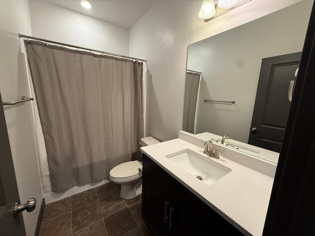 Bathroom featuring a dark wood-finish vanity with a white countertop and integrated sink, brushed nickel faucet, large wall mirror, and tile flooring
